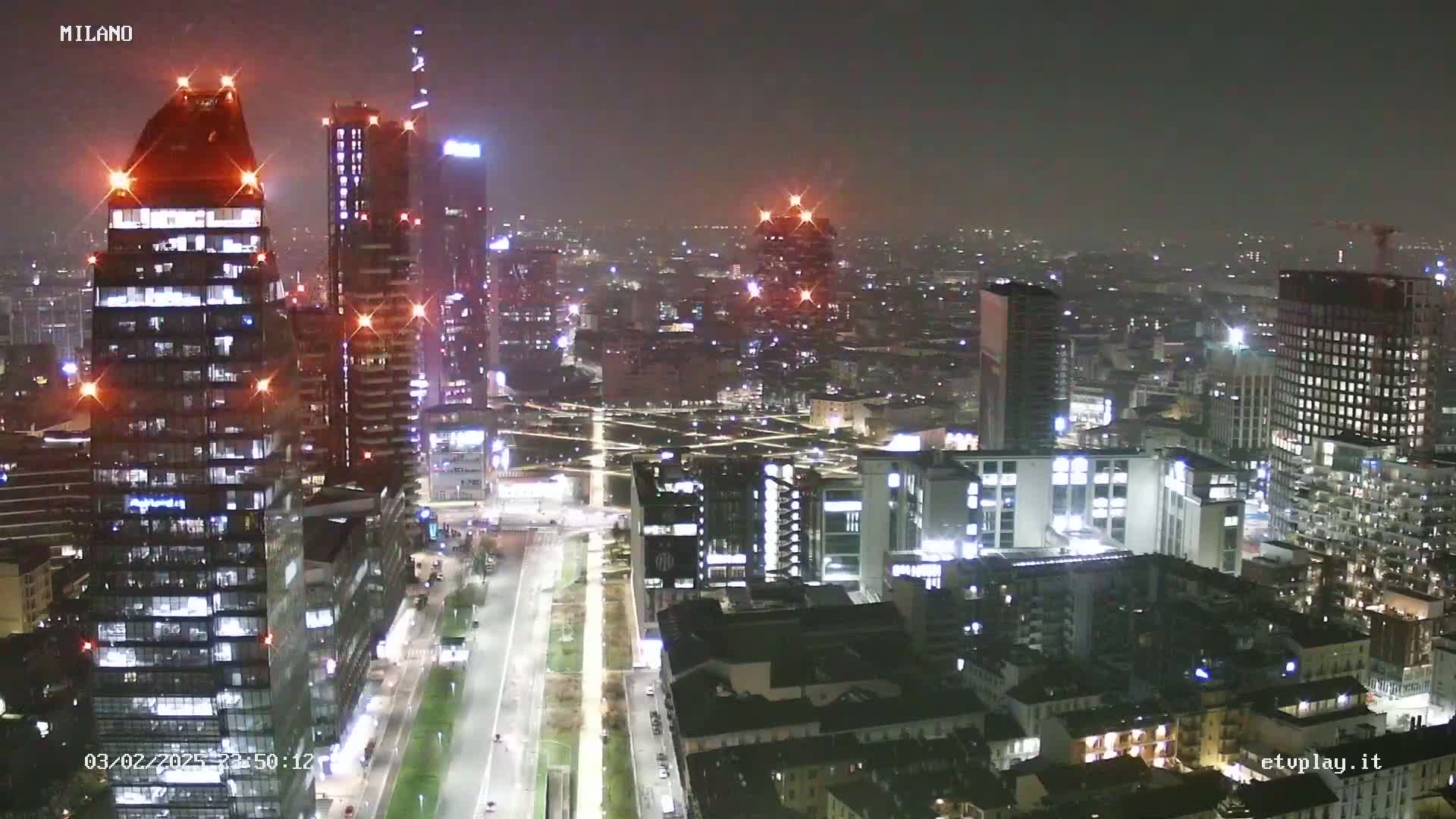 A nighttime aerial view of a city skyline showing many illuminated skyscrapers and buildings under hazy conditions.