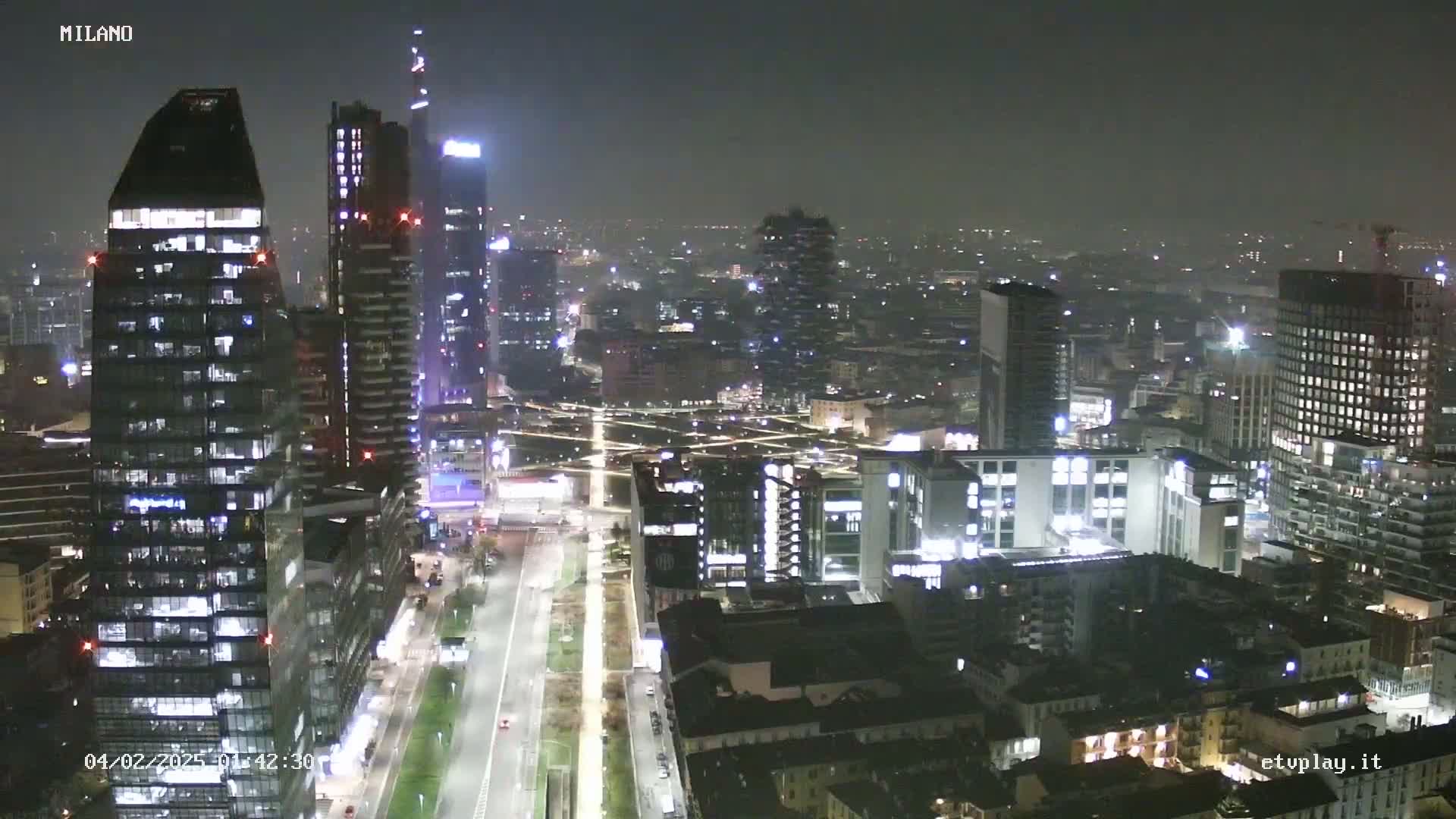 A nighttime aerial view of a city skyline with many tall buildings lit up under hazy conditions.