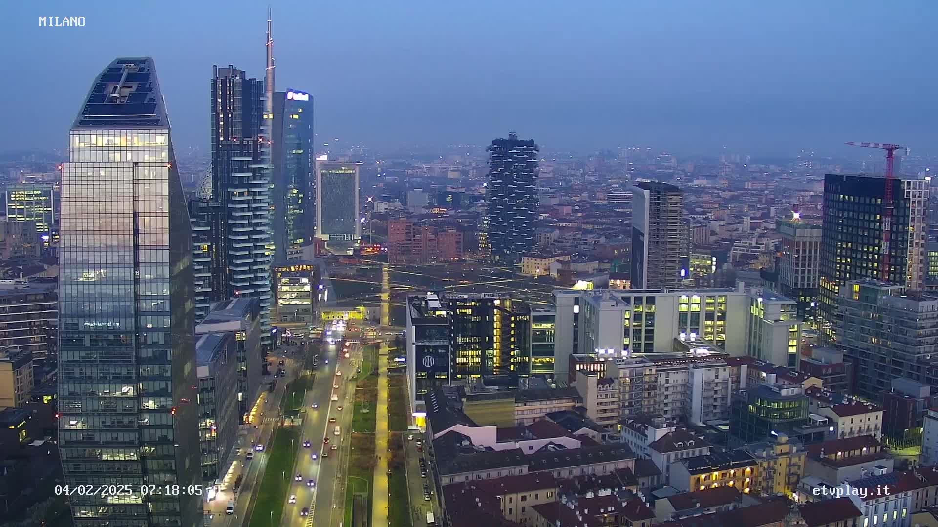 A nighttime aerial view of a city skyline with numerous skyscrapers and high-rise buildings, under a hazy, dusky sky.