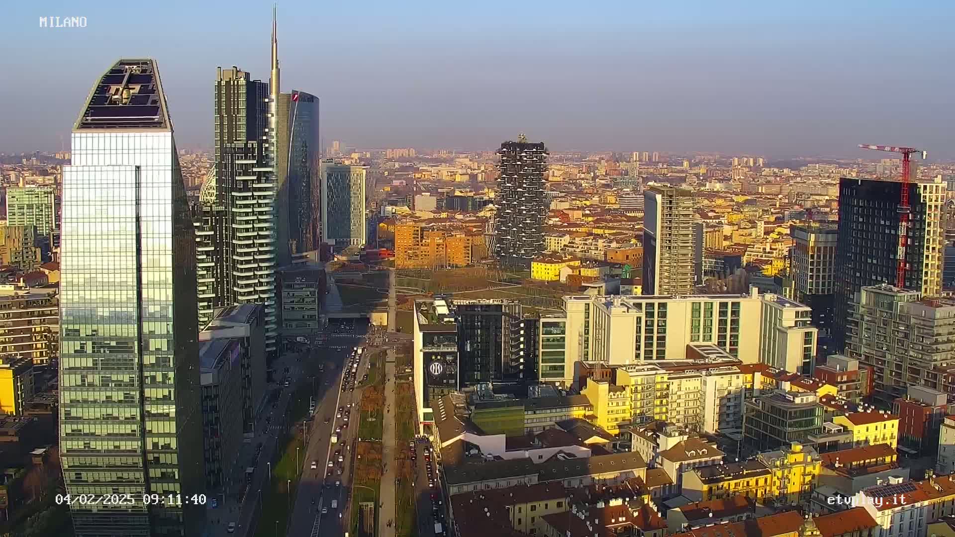 An aerial view of a city skyline with many modern skyscrapers under a clear, hazy sky.