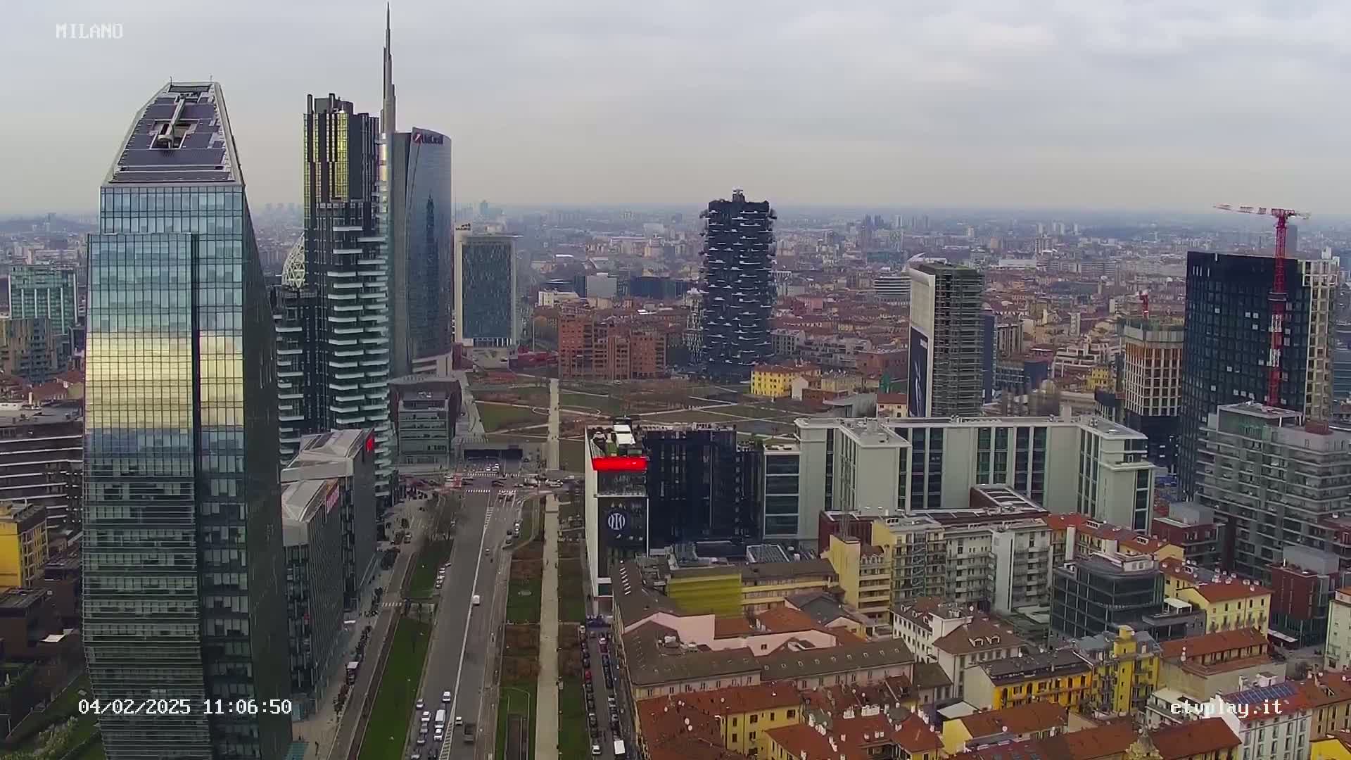 An aerial view of a city with numerous skyscrapers under an overcast sky shows a highway cutting through the urban landscape.