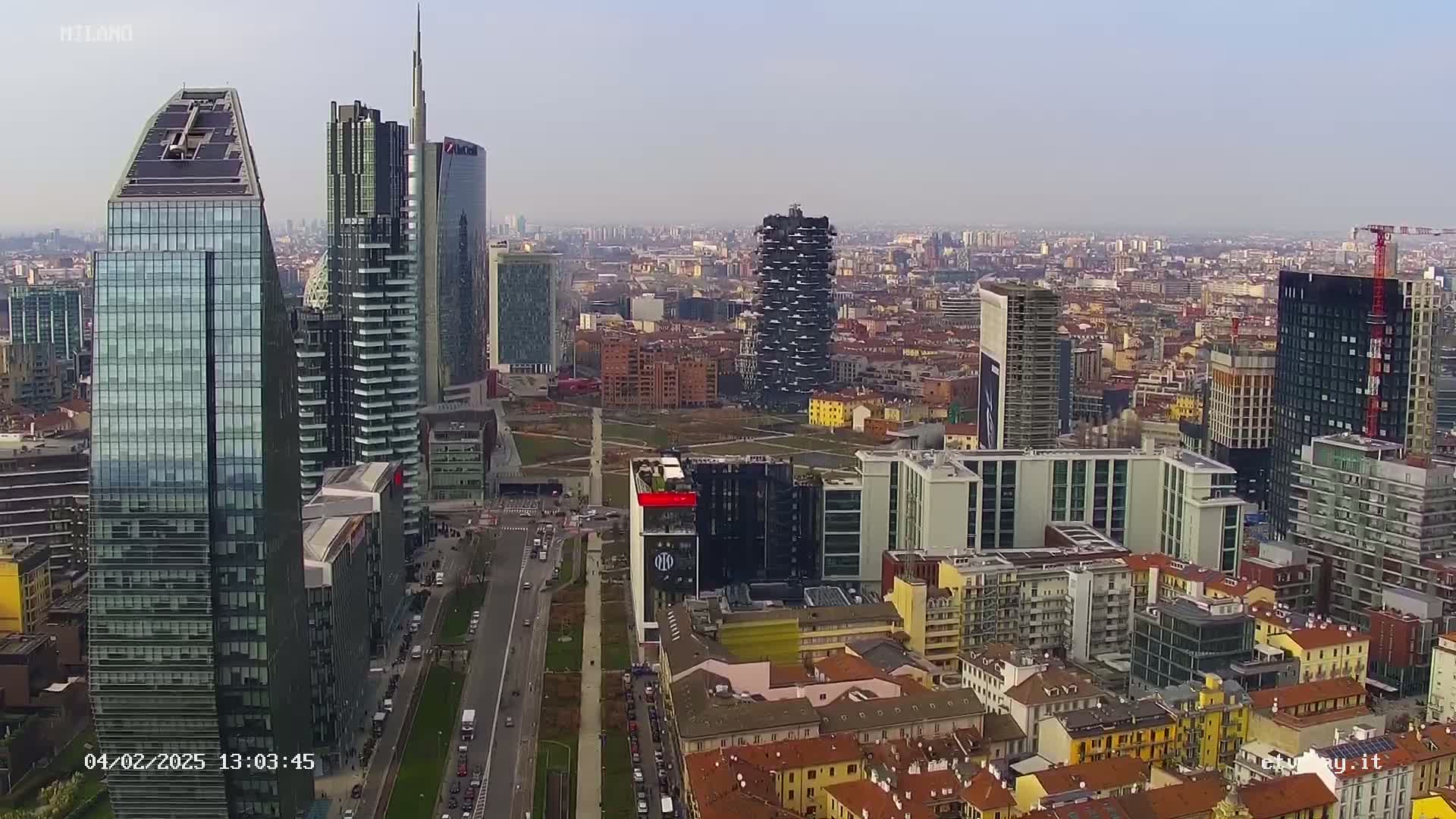 A high-angle, long shot of a city skyline on a clear day, showing numerous modern skyscrapers and surrounding low-rise buildings.