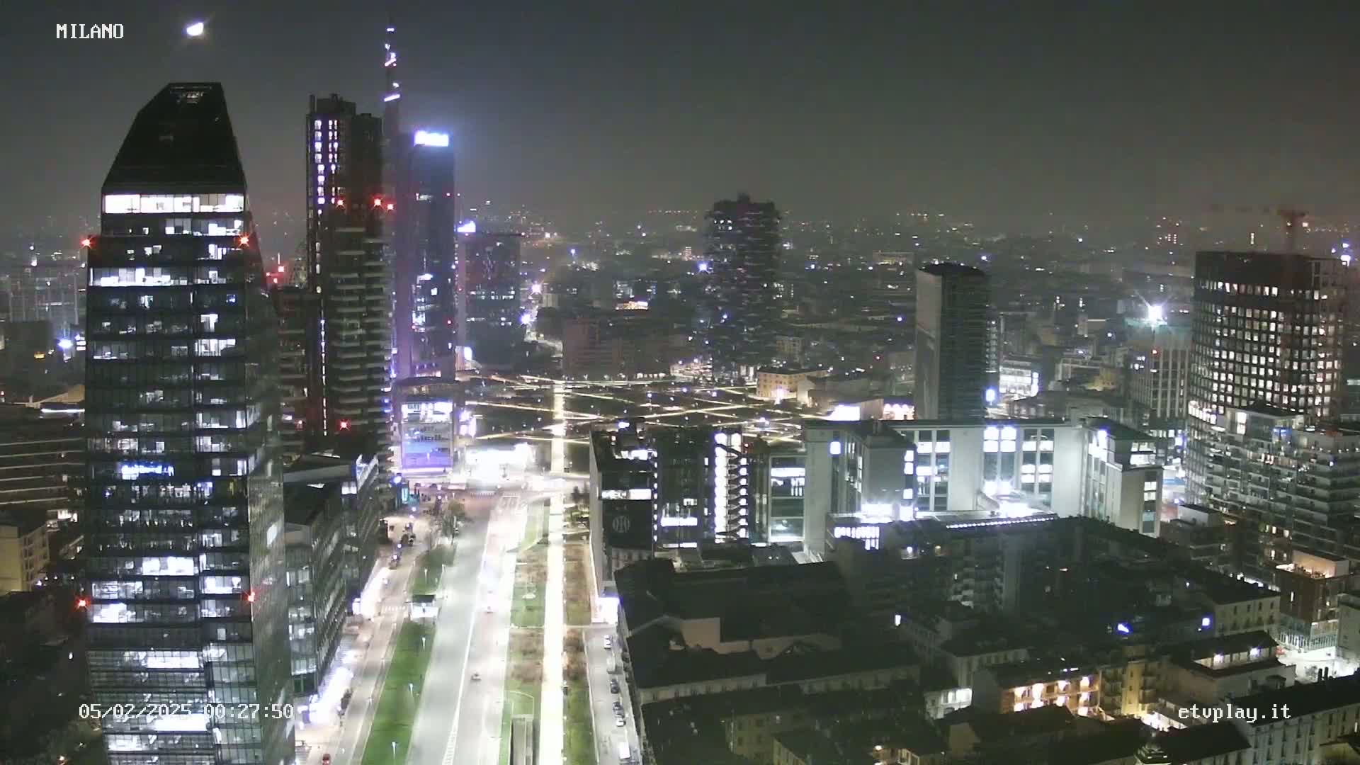A nighttime aerial view of a city with numerous illuminated skyscrapers and buildings, under hazy or foggy conditions.