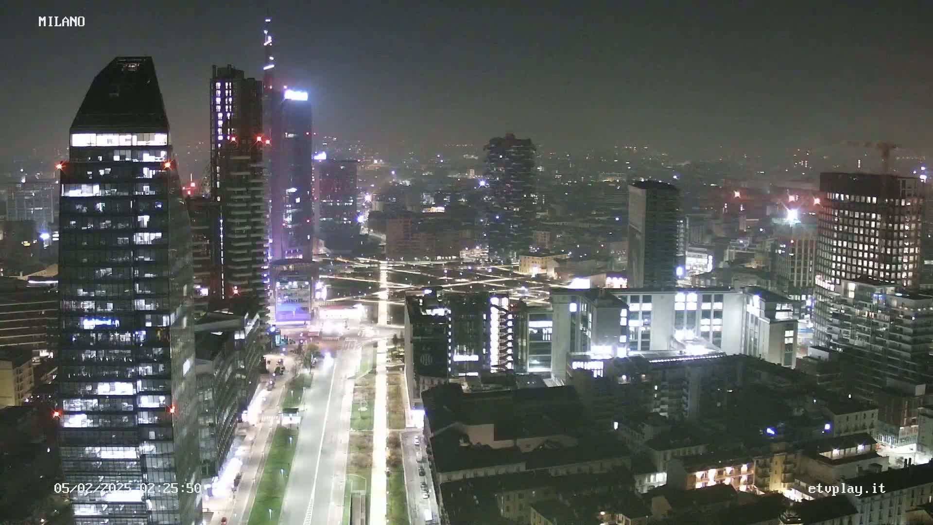 A nighttime aerial view of a city skyline with numerous skyscrapers and illuminated buildings, under hazy conditions.