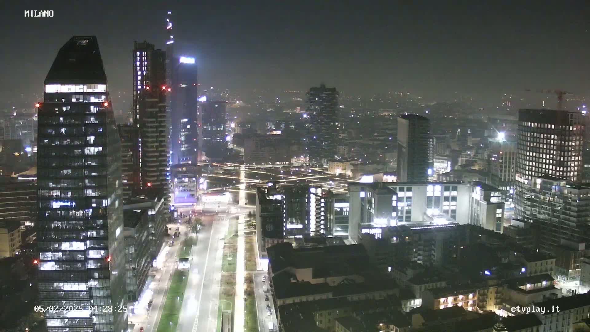 A nighttime aerial view of a city's skyline, showing numerous illuminated skyscrapers and buildings under hazy conditions.