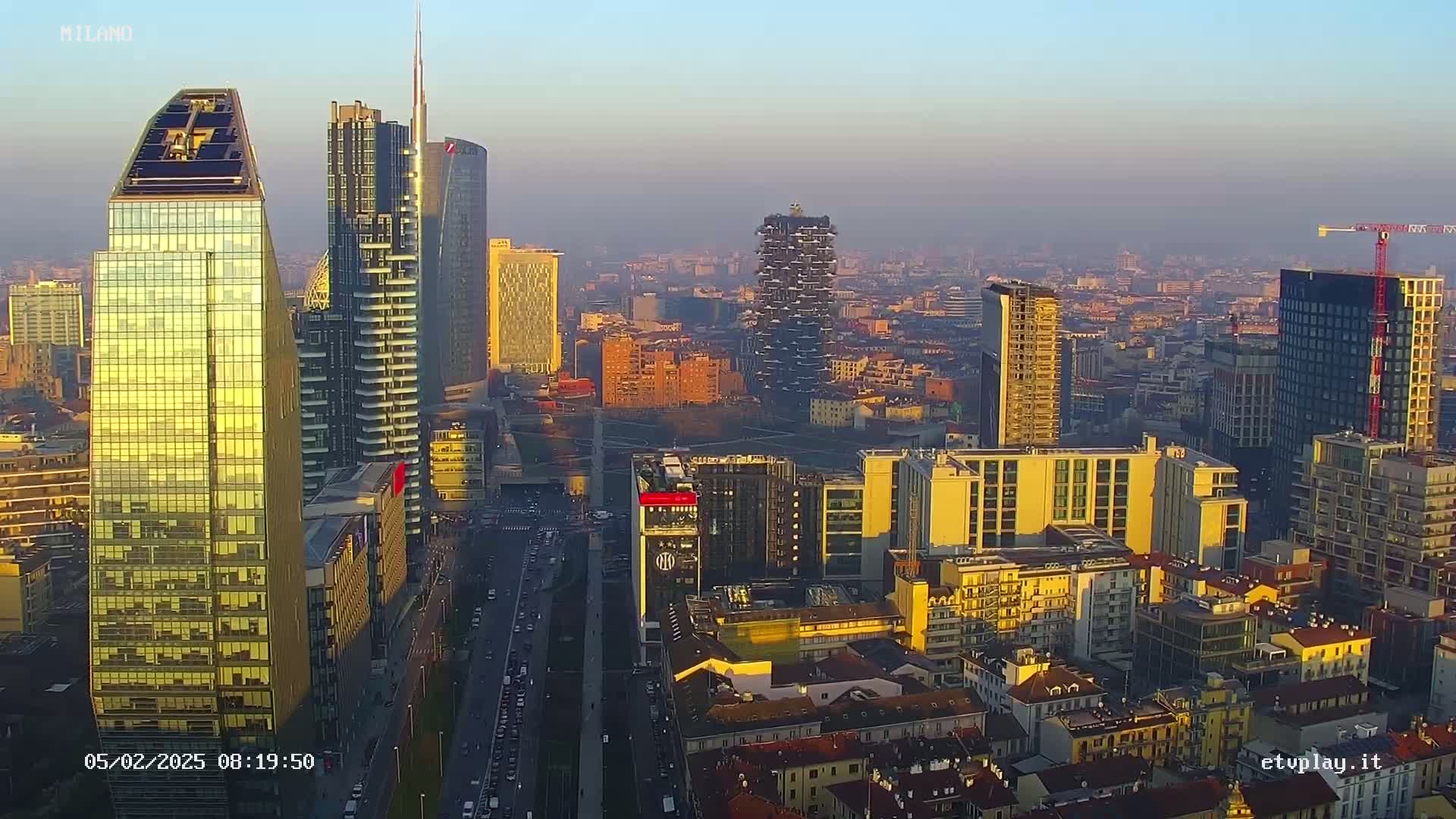 An aerial view of a city skyline at sunrise, with hazy weather conditions and numerous skyscrapers, some under construction.