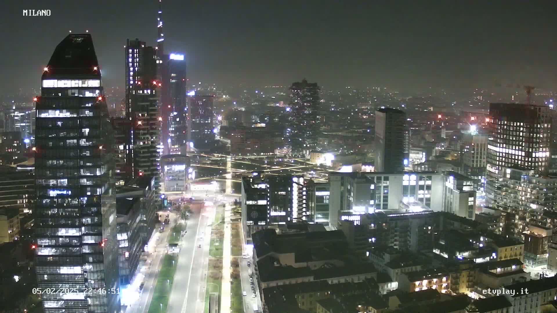 A nighttime aerial view of a city with many illuminated skyscrapers and buildings under hazy conditions.