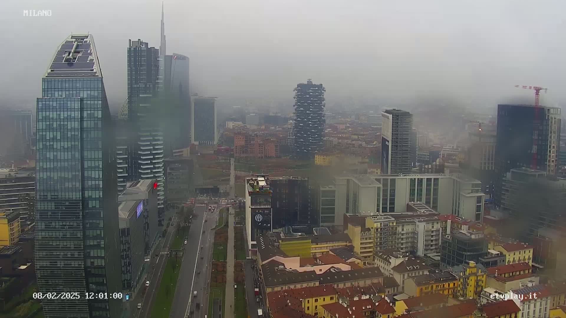 A foggy view of a city skyline featuring numerous skyscrapers and high-rise buildings, with a road visible in the foreground.