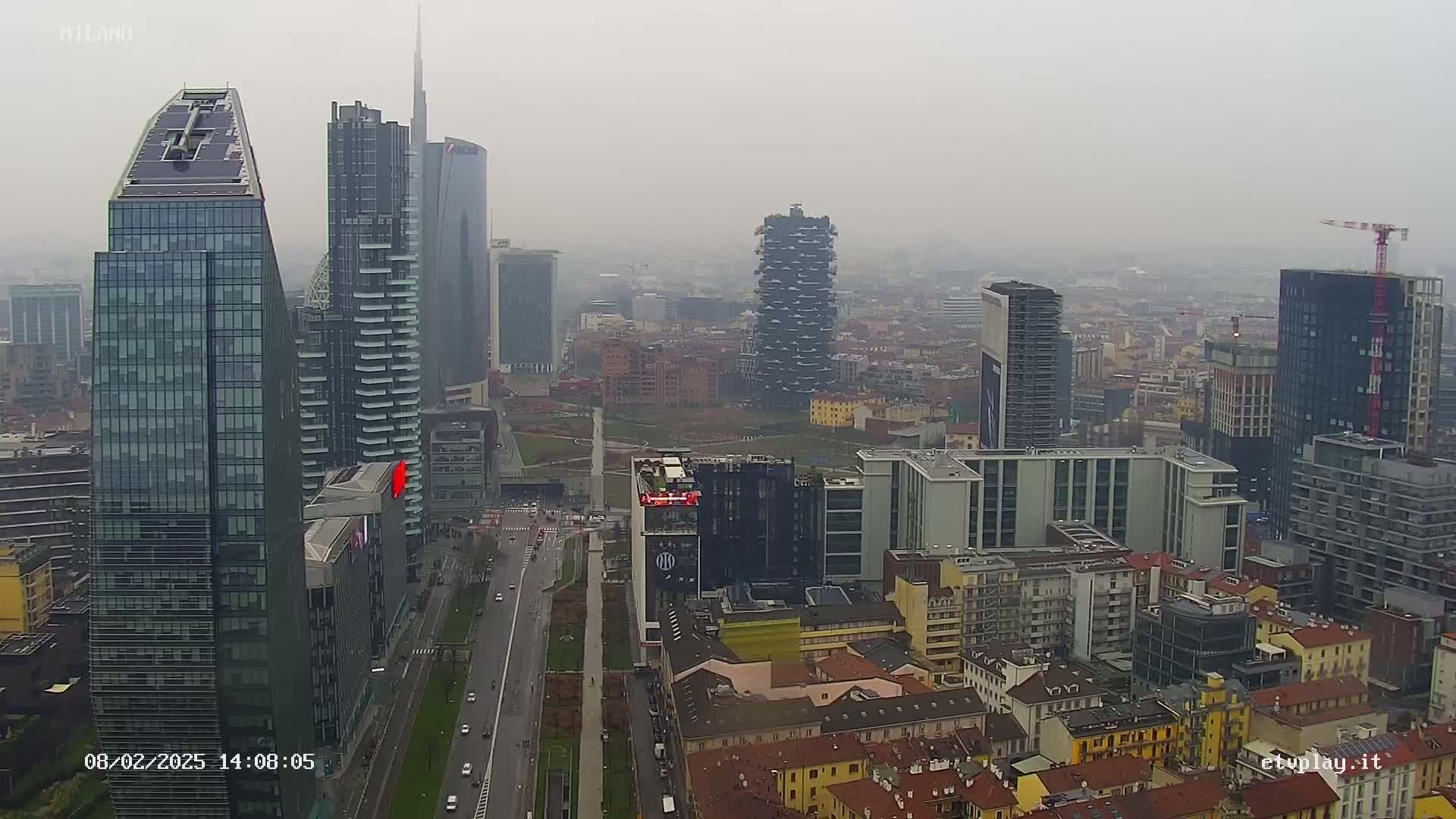 A hazy cityscape of numerous high-rise buildings and a wide street, viewed from above on an overcast day.