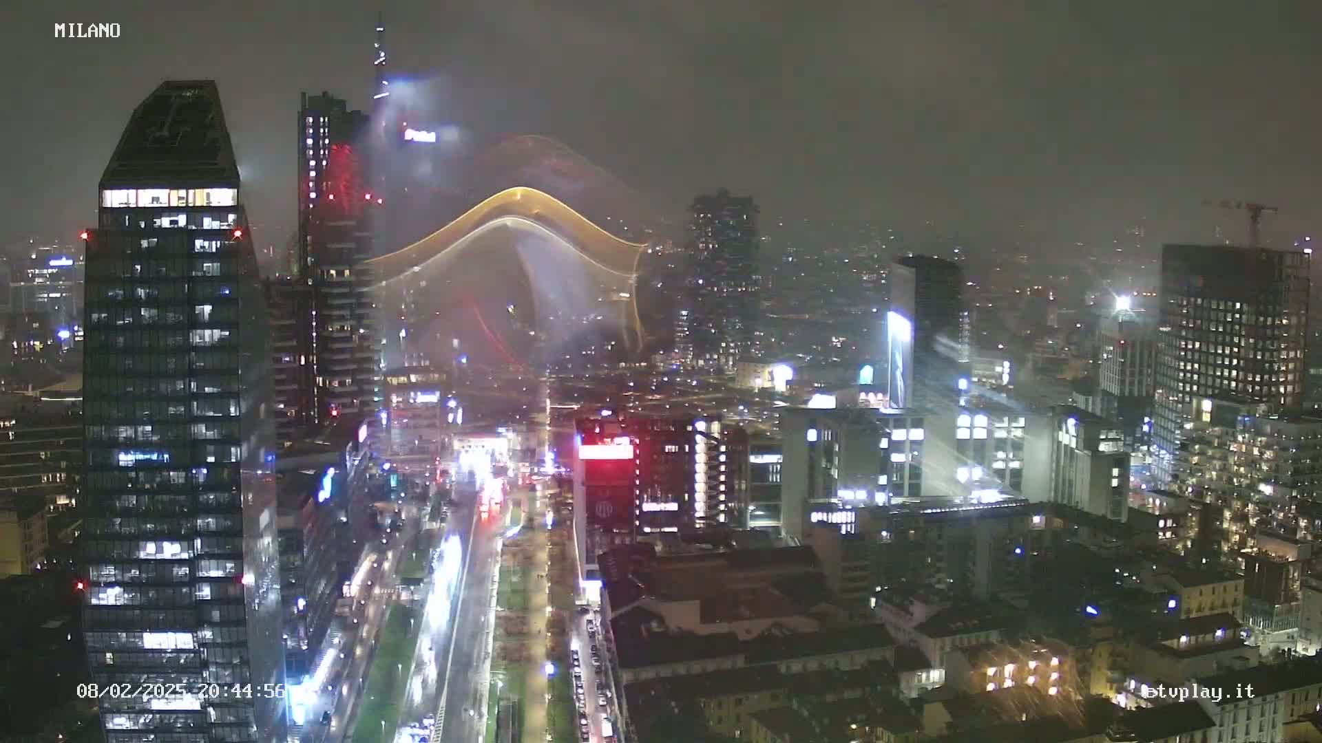 A nighttime, rain-swept view of a city skyline showing numerous illuminated skyscrapers and streets.