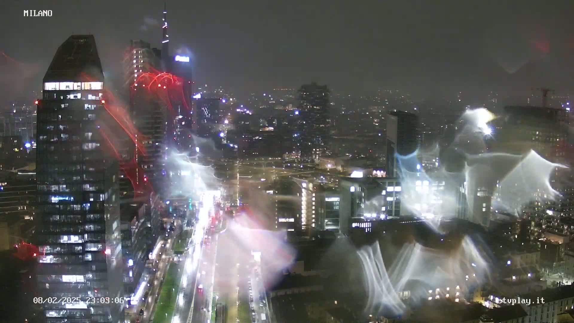 A nighttime view of a city, possibly during a rain or snowstorm, shows illuminated skyscrapers and city streets with blurry streaks of light from precipitation or camera effects.