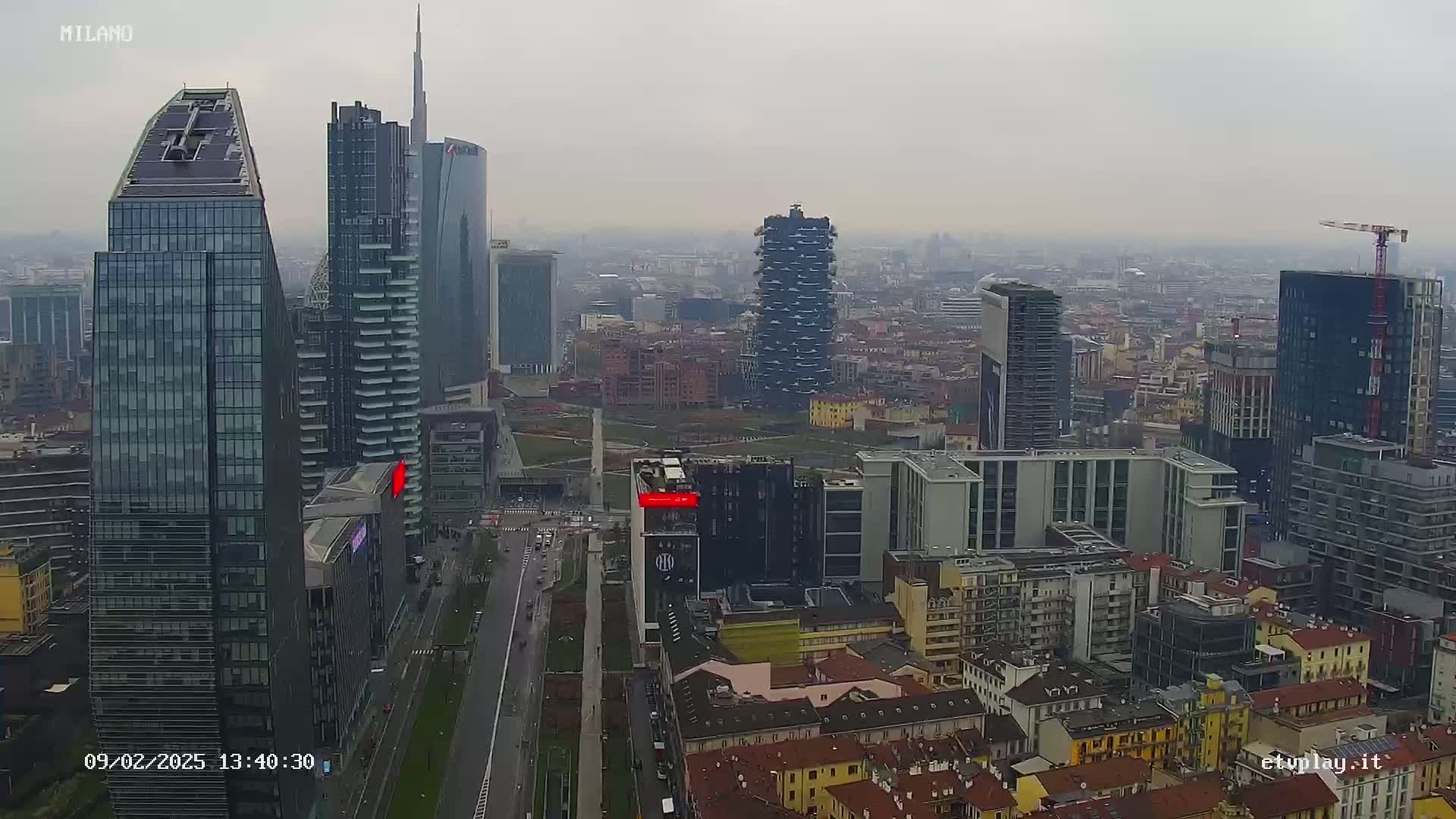 A high-angle, long shot of a city skyline on an overcast day, featuring numerous skyscrapers and surrounding buildings.