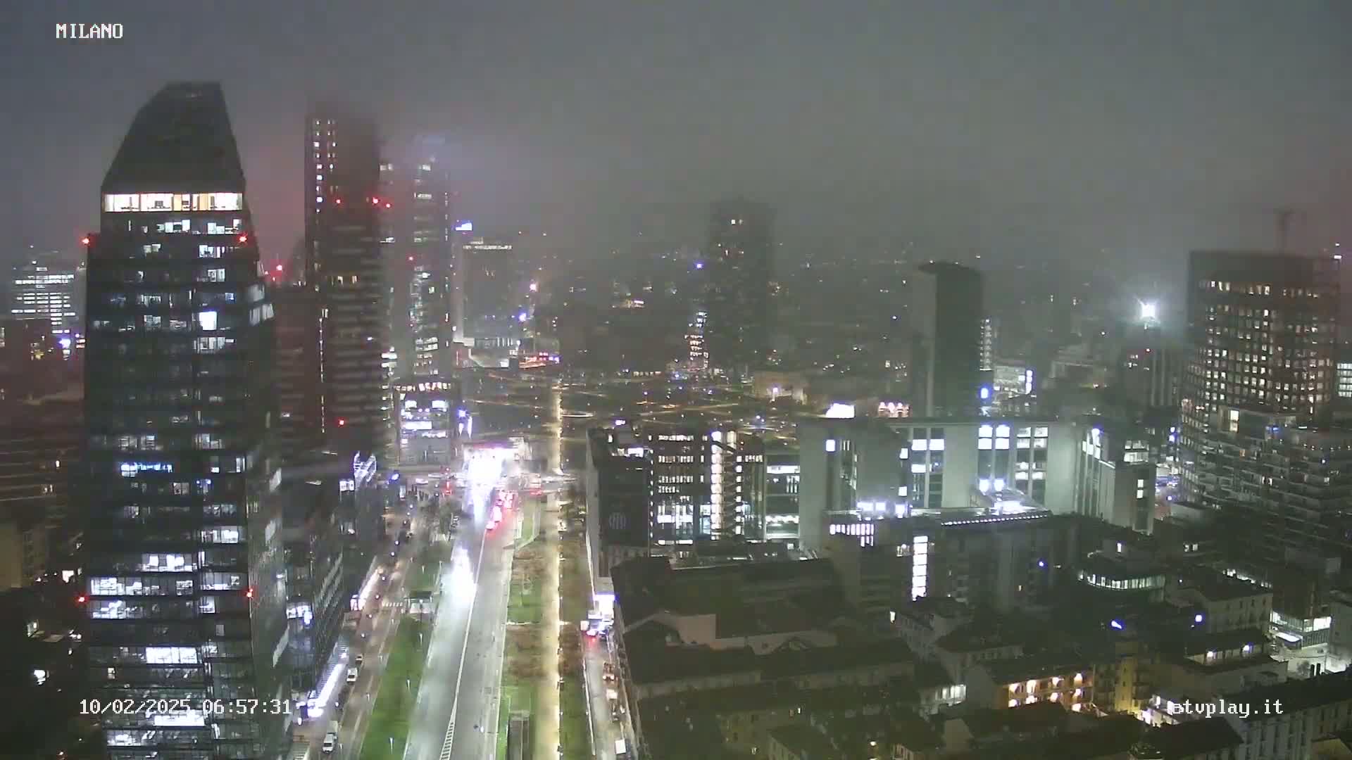 A nighttime cityscape of numerous illuminated skyscrapers and buildings under foggy conditions.