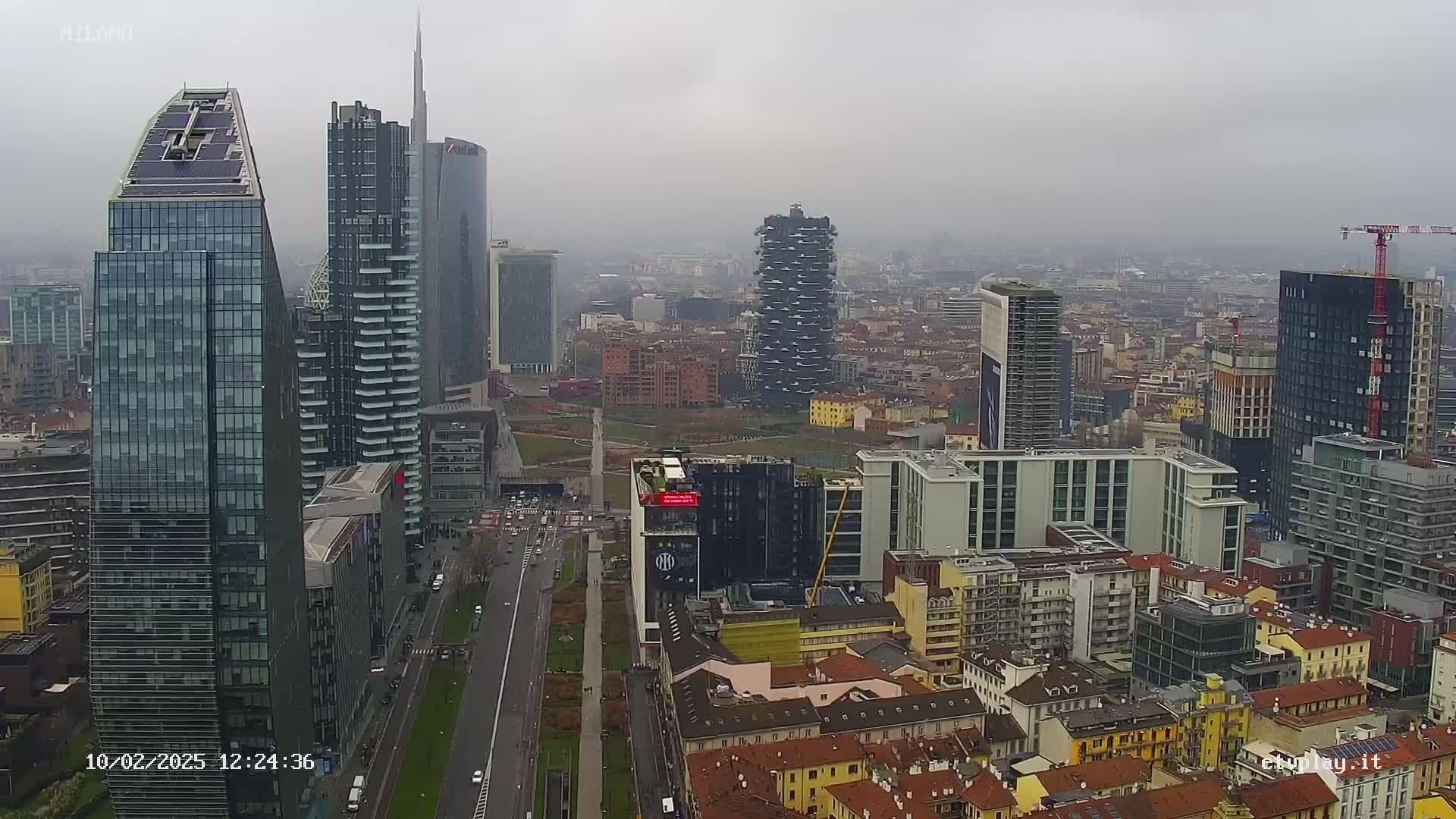 A hazy, overcast day reveals a cityscape of numerous skyscrapers and high-rise buildings, with a wide street running through the foreground.