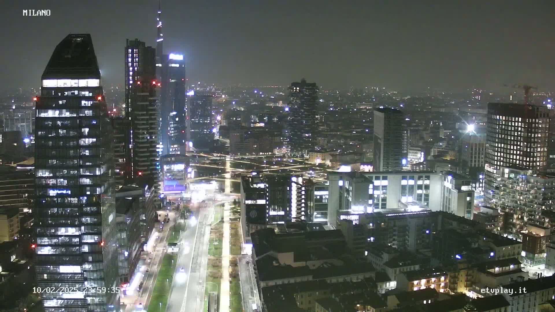 A nighttime aerial view of a city skyline, showing numerous illuminated buildings and streets under hazy conditions.