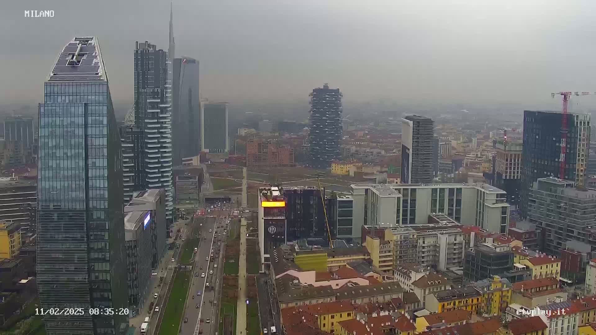 A hazy aerial view of a city skyline featuring numerous modern skyscrapers and surrounding buildings under overcast skies.
