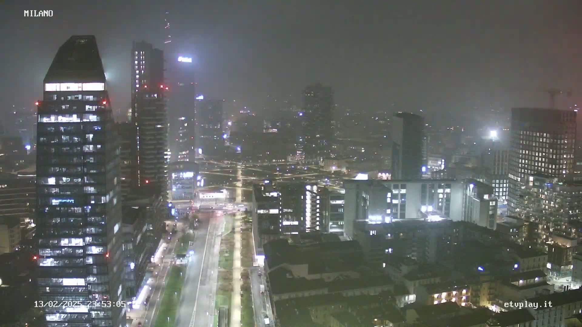 A nighttime cityscape of numerous illuminated buildings under a foggy sky.