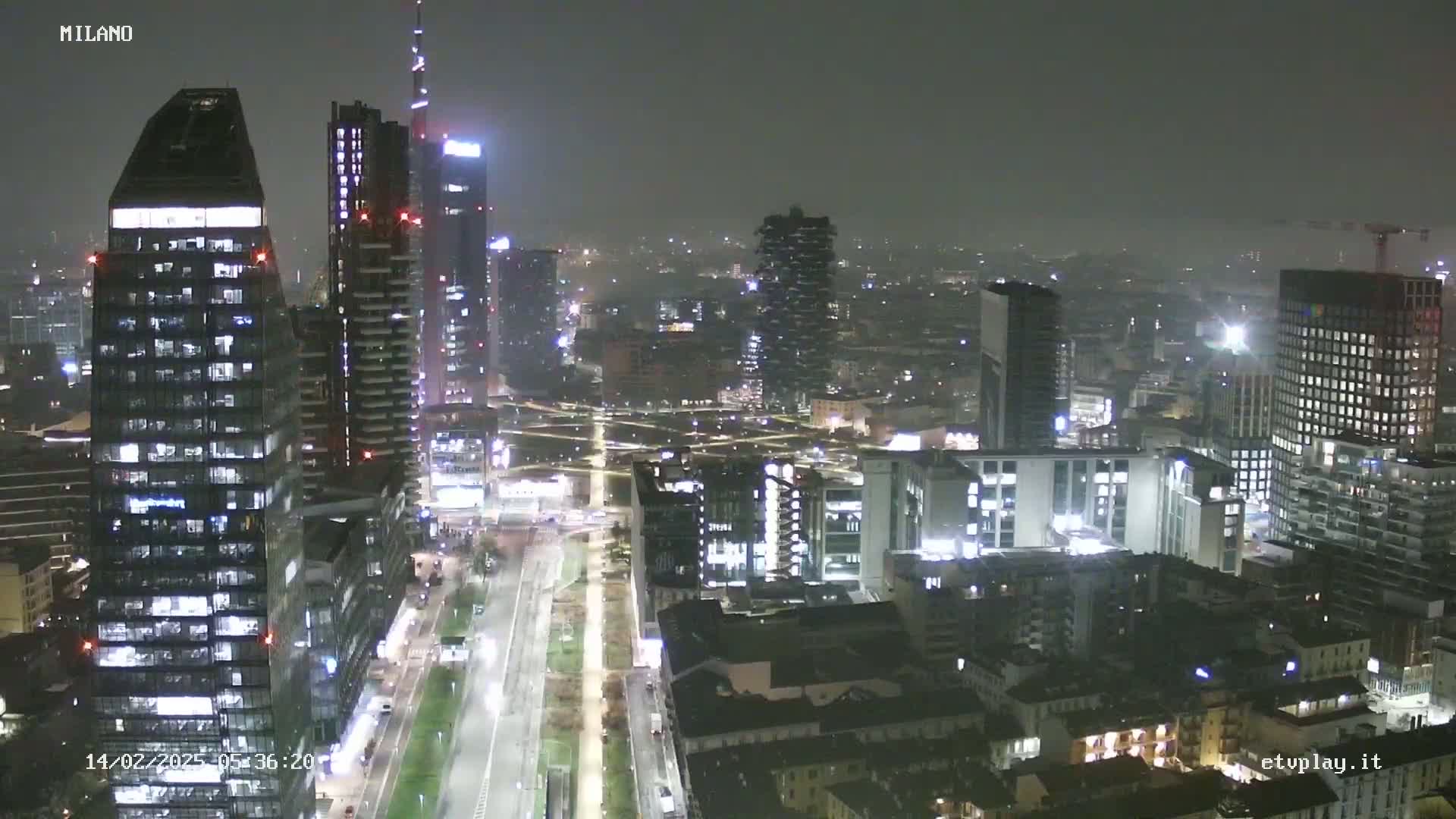 A nighttime view of a city skyline showing numerous illuminated skyscrapers and buildings under hazy or foggy conditions.