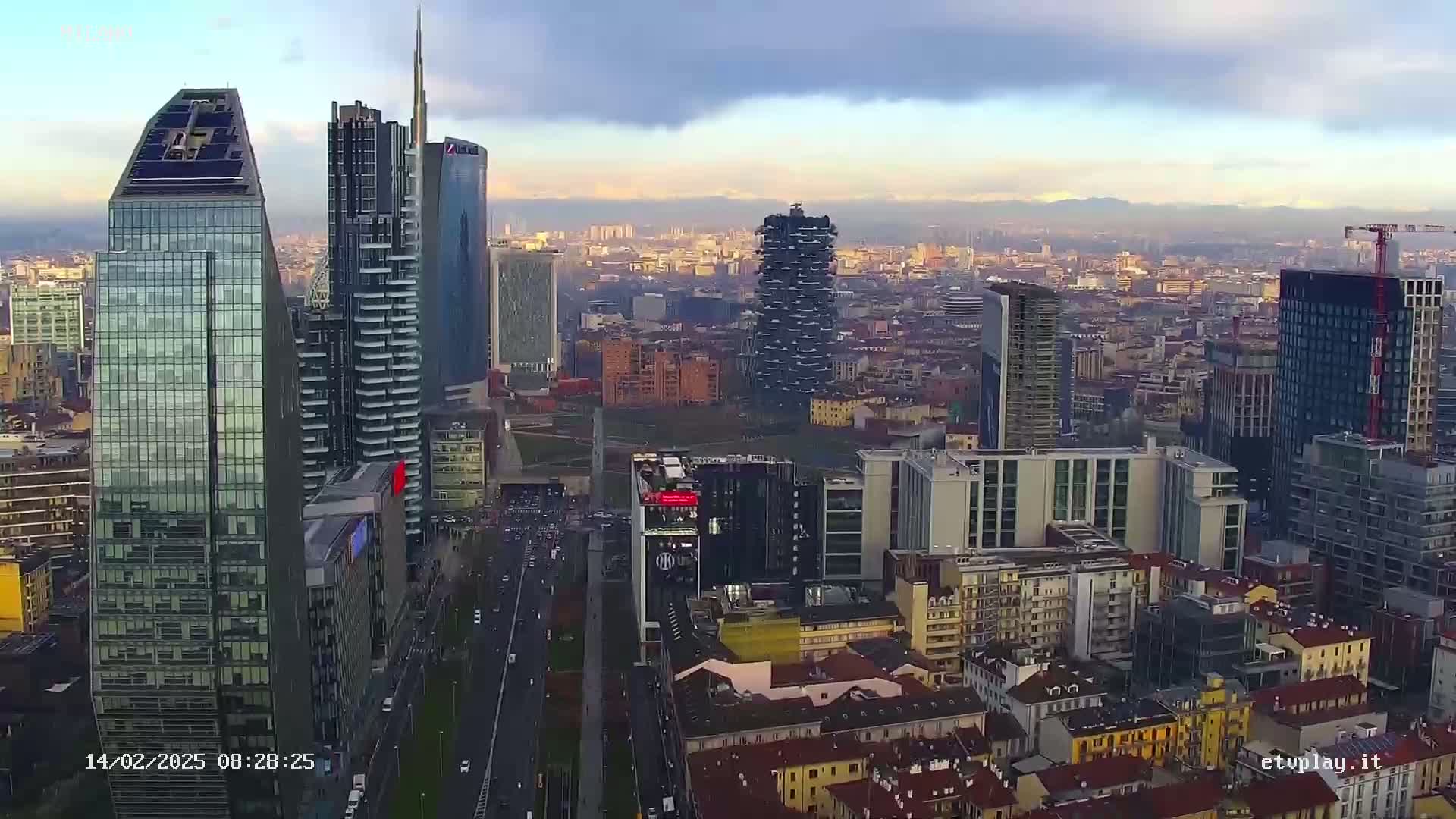 An aerial view of a city skyline with numerous skyscrapers under a partly cloudy sky.