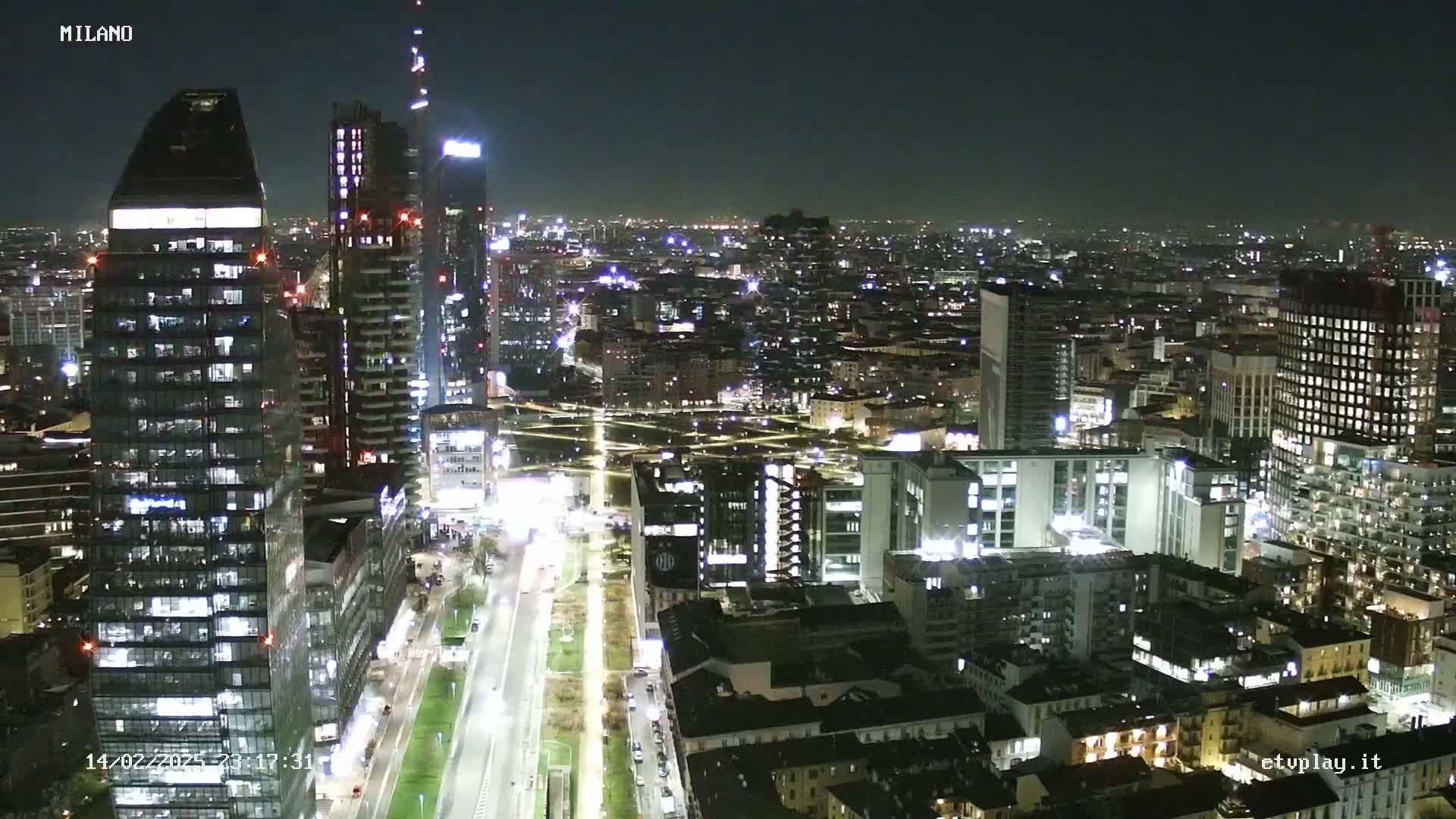 A nighttime aerial view of a densely populated city with numerous illuminated buildings, streets, and roads.