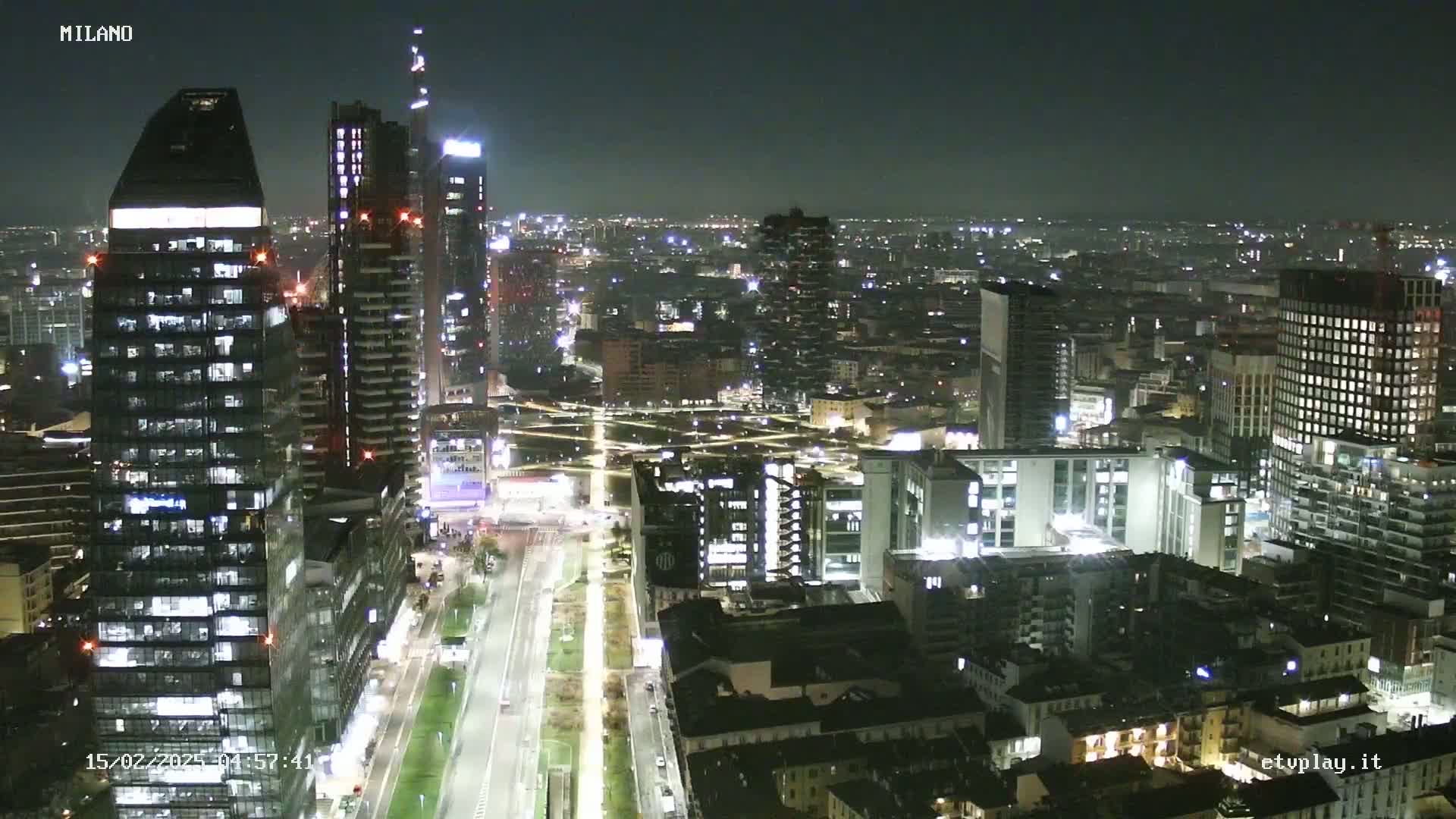 A nighttime aerial view of a city skyline shows numerous illuminated buildings and streets, with clear skies.