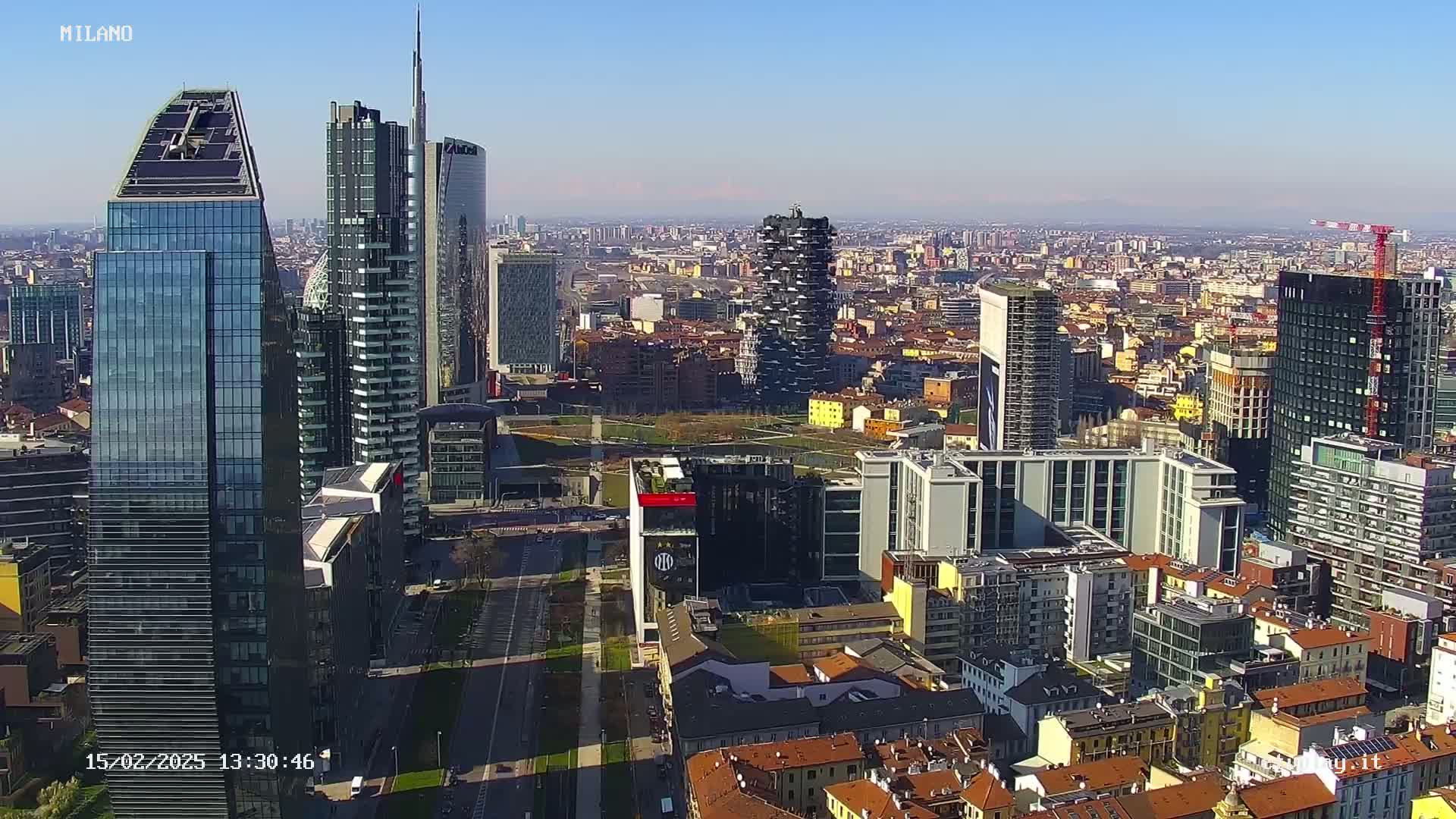 A high-angle, long shot of a city skyline on a clear, sunny day, showing many modern skyscrapers and surrounding buildings.