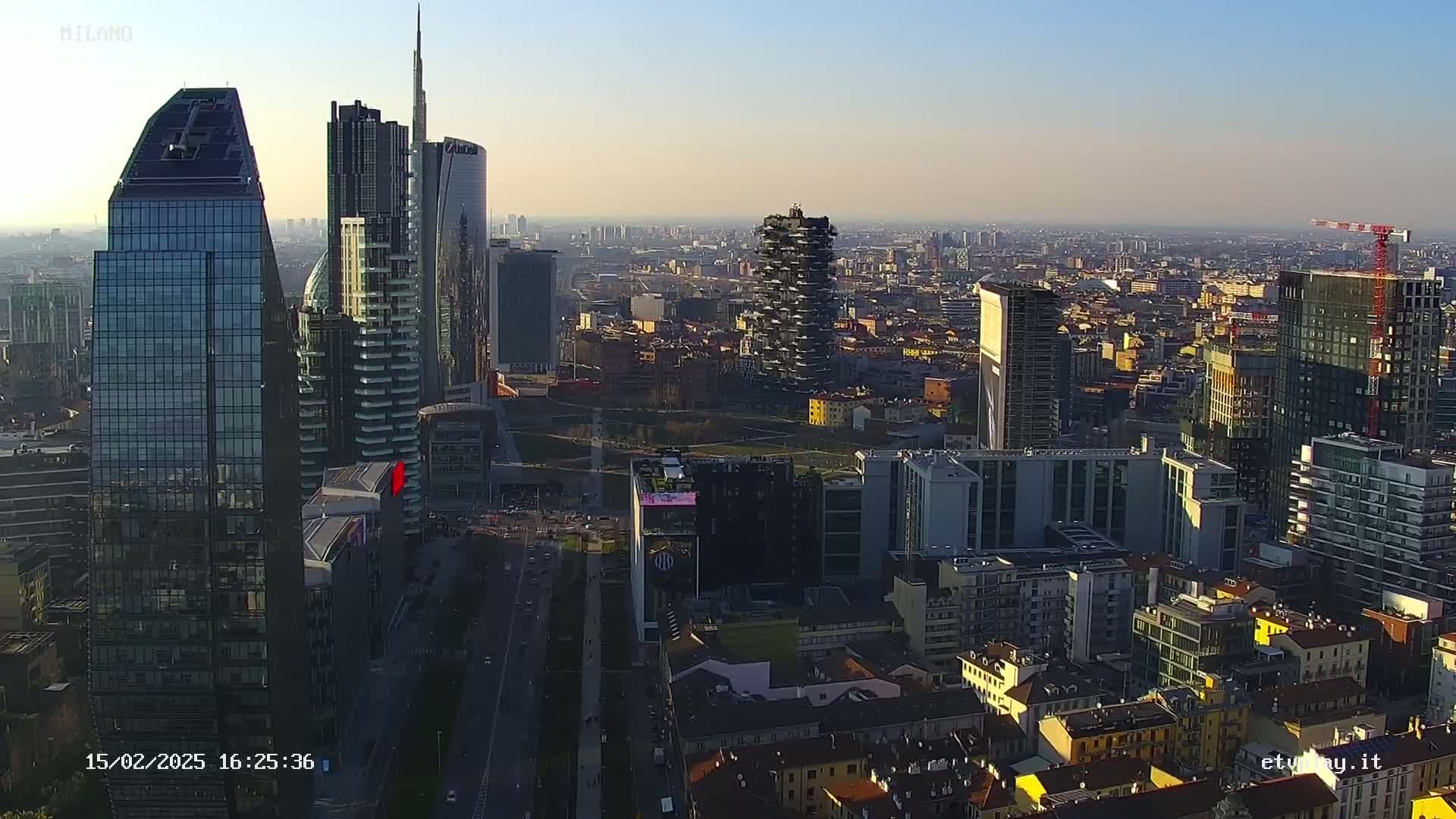 An aerial view of a dense cityscape with numerous skyscrapers under a clear, bright sky.