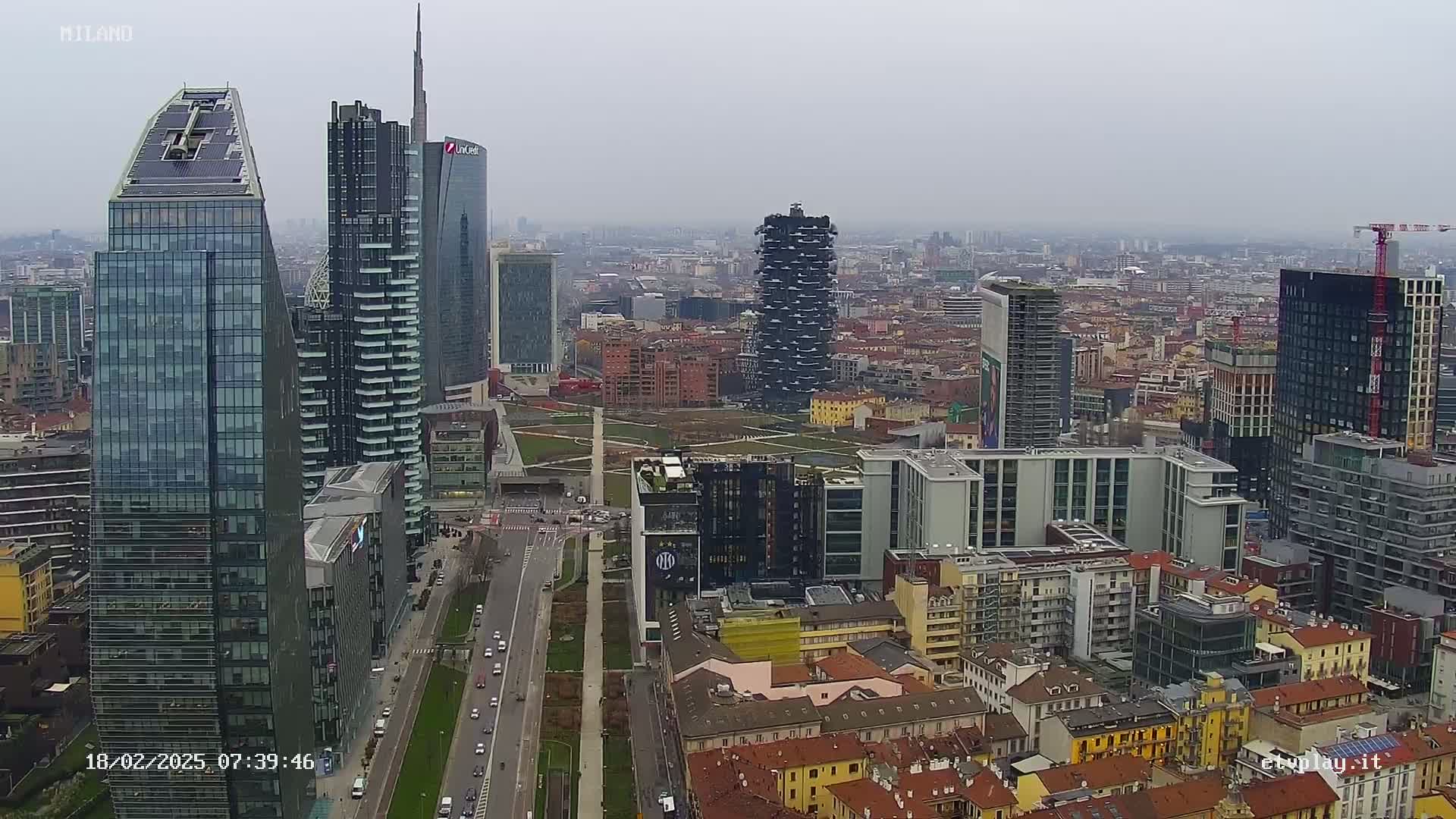A high-angle, long shot of a city skyline on an overcast day, showing numerous skyscrapers and surrounding buildings, with a highway running through the scene.