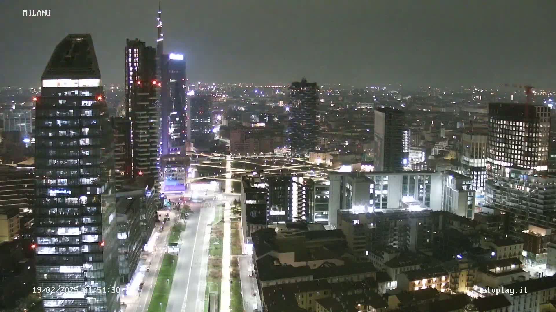 A nighttime aerial view of a city skyline showing numerous skyscrapers and buildings illuminated under a dark sky.