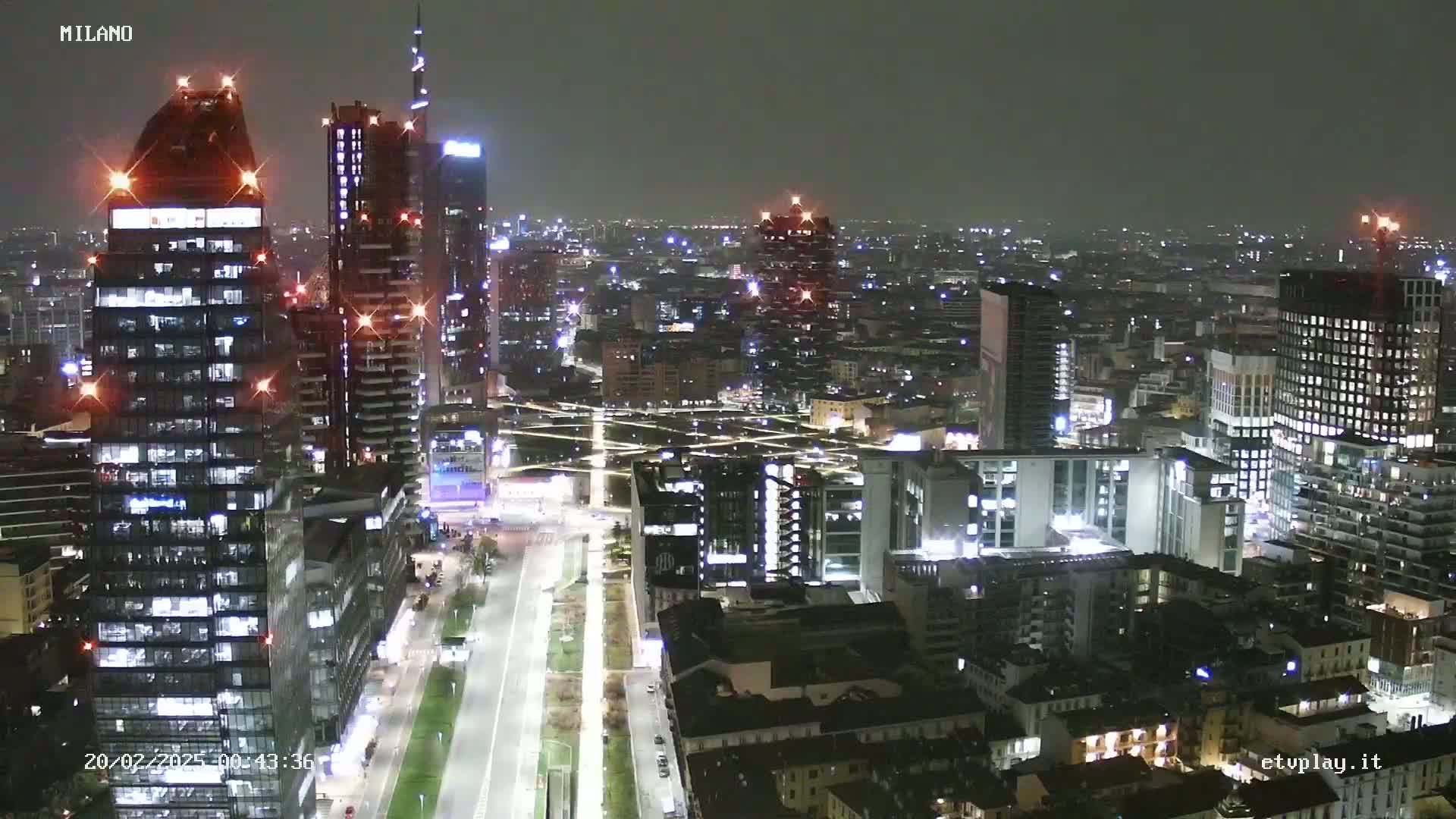 A nighttime aerial view of a city with numerous illuminated skyscrapers and buildings, under a dark sky.