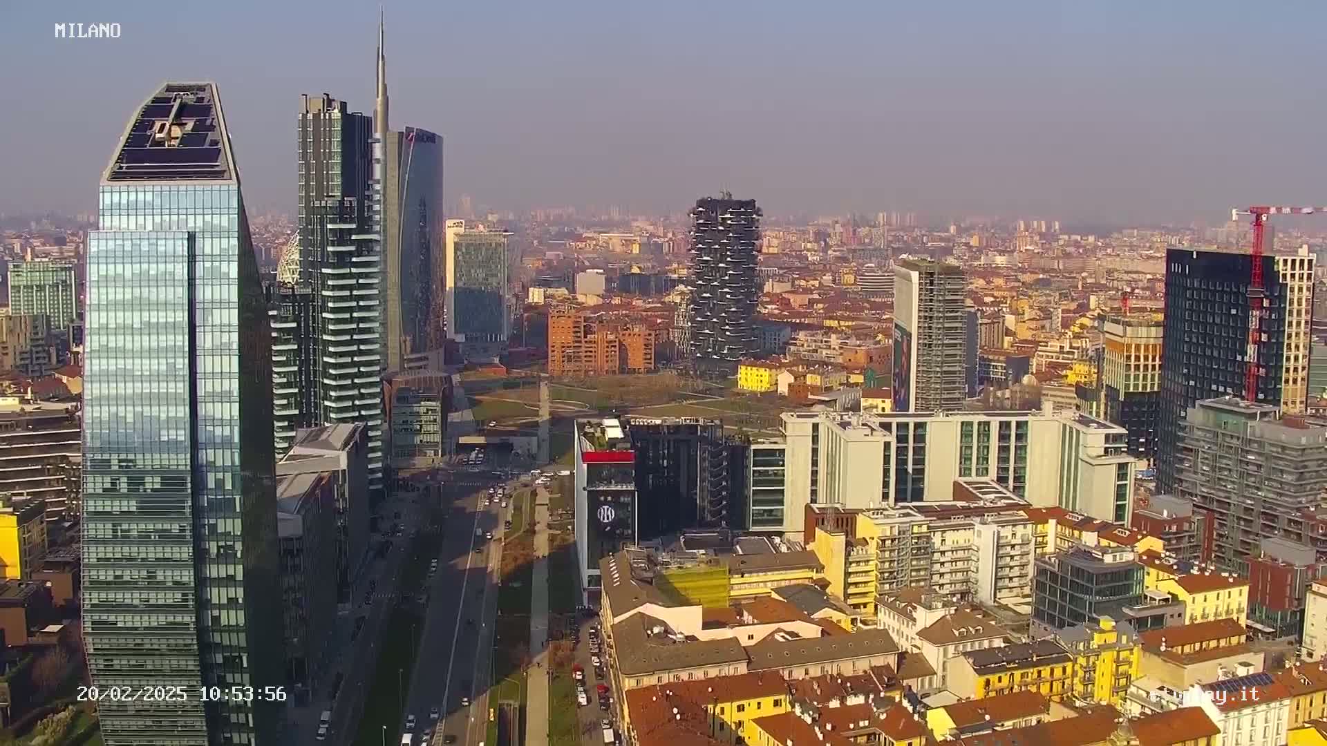 An aerial view of a city skyline on a sunny day, showing numerous skyscrapers and surrounding buildings.