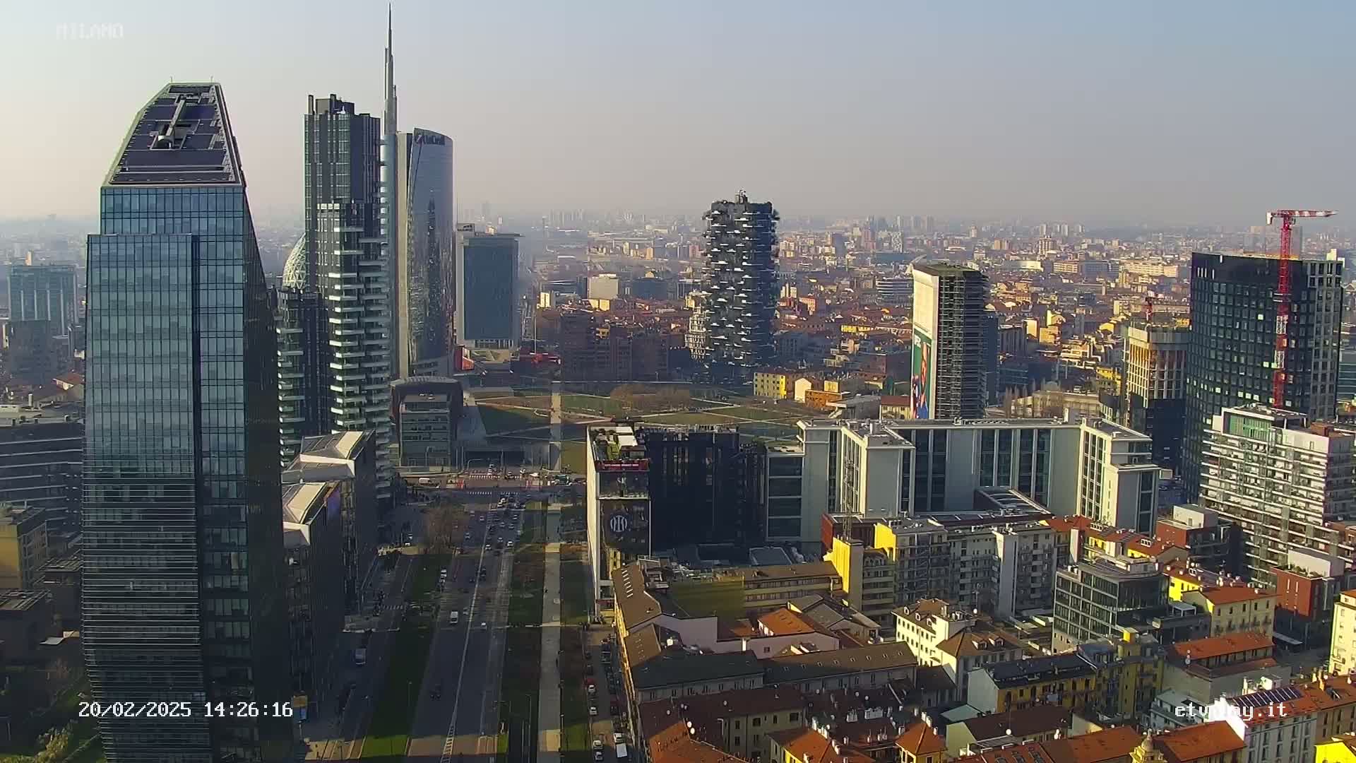A hazy, sunny day reveals a dense cityscape of modern skyscrapers and traditional buildings, viewed from an elevated perspective.