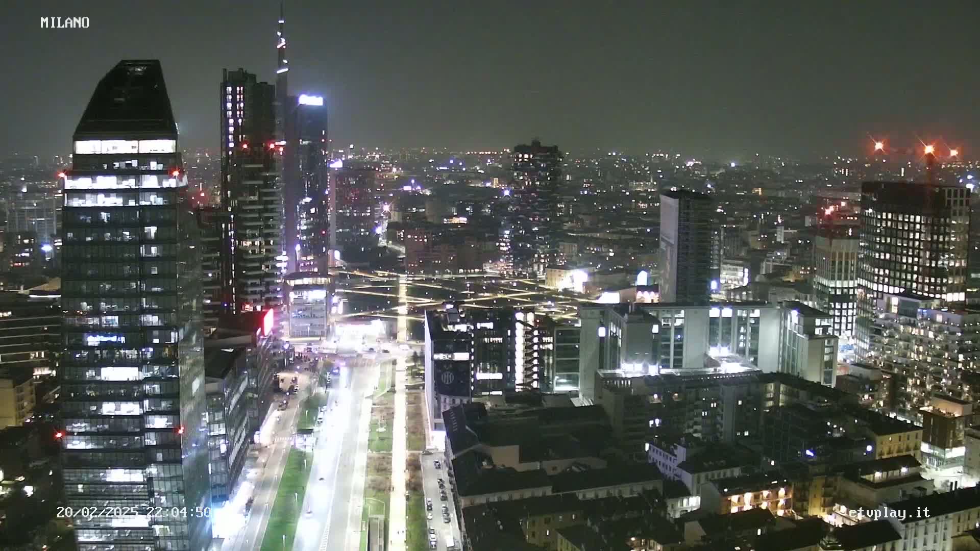 A nighttime aerial view of a city, showing numerous illuminated skyscrapers and buildings, with a mostly clear sky.