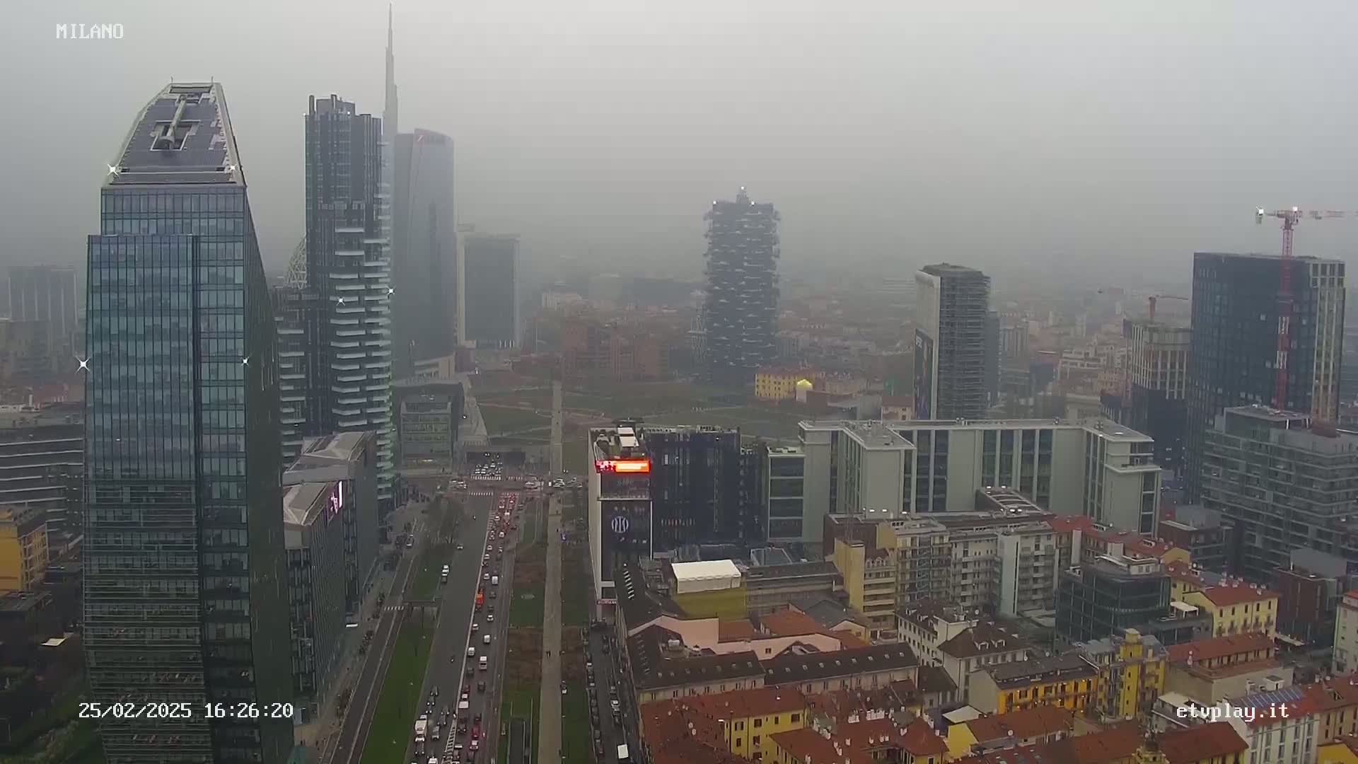 A hazy, overcast view of a city skyline featuring numerous skyscrapers and surrounding buildings, with a road visible below.