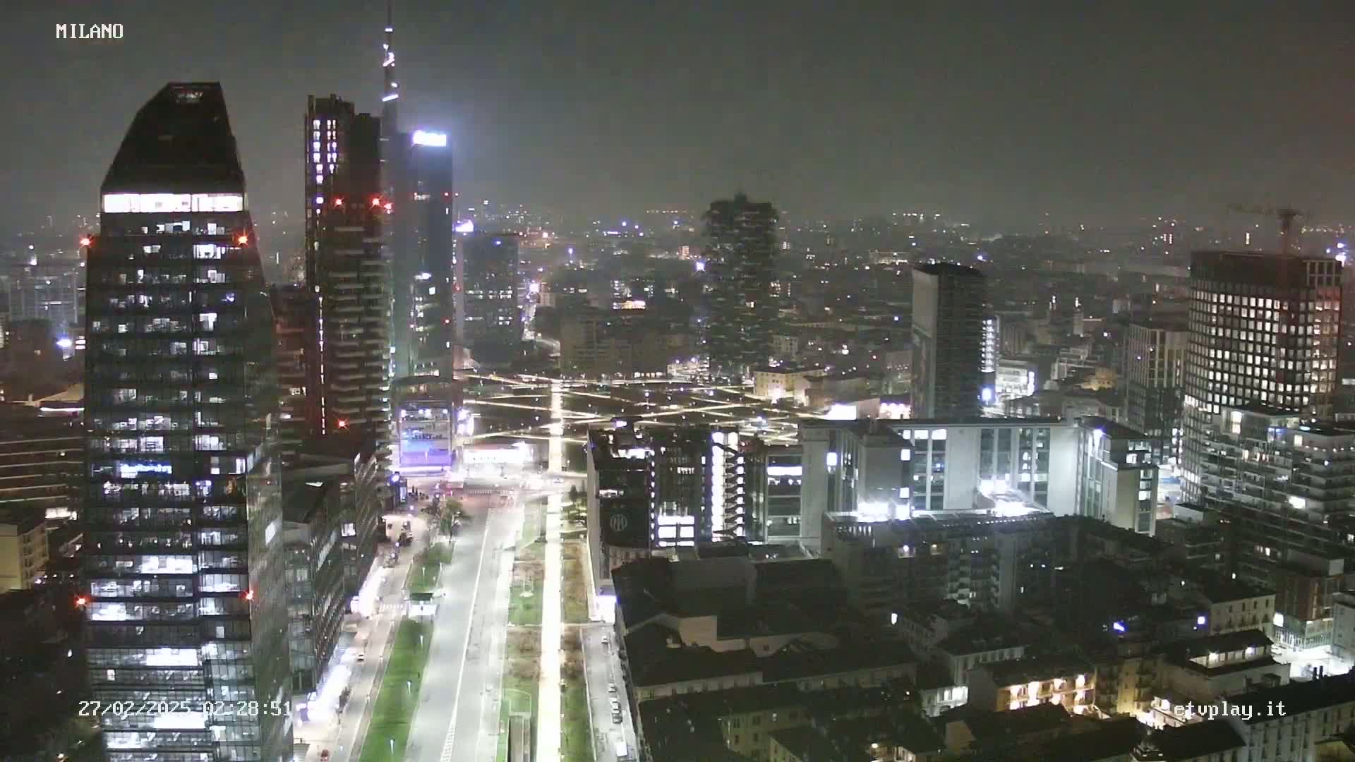 A nighttime view of a city skyline with many skyscrapers and streets, under hazy or foggy conditions.