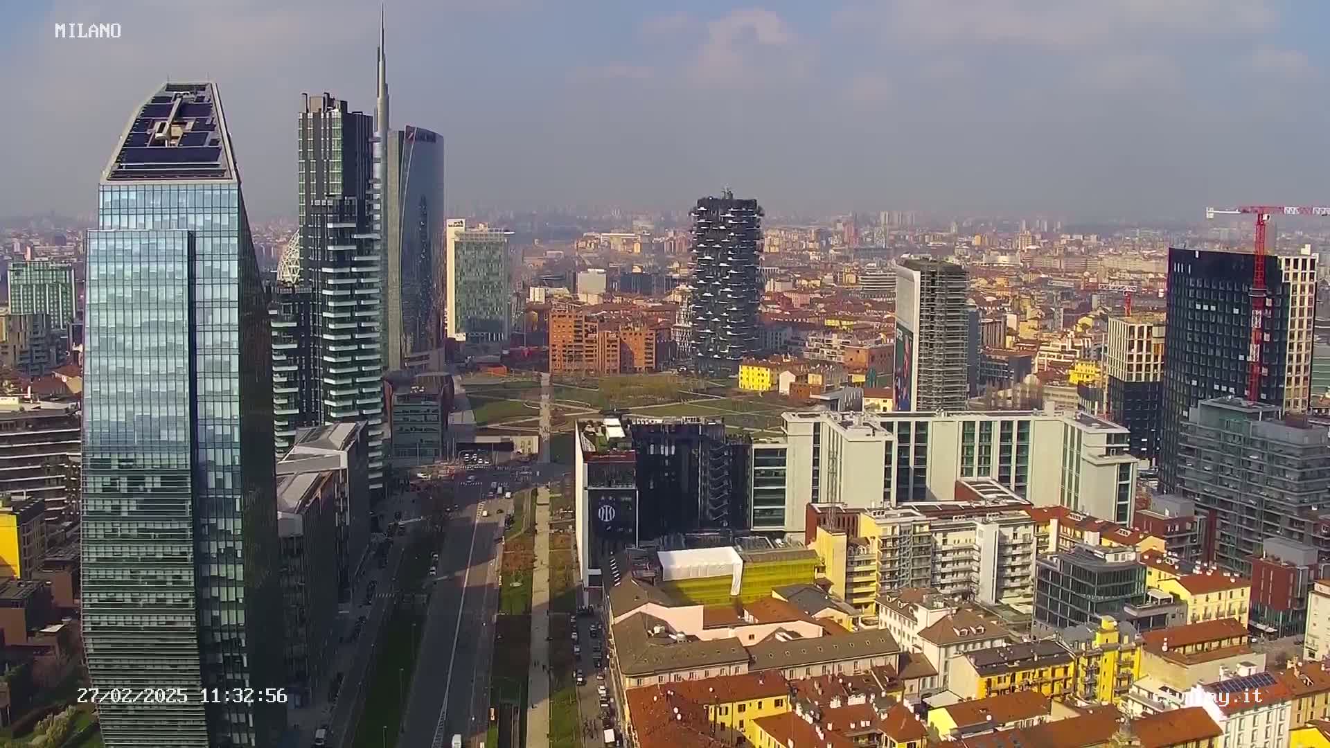 An aerial view of a city with numerous skyscrapers, under a mostly clear, sunny sky.