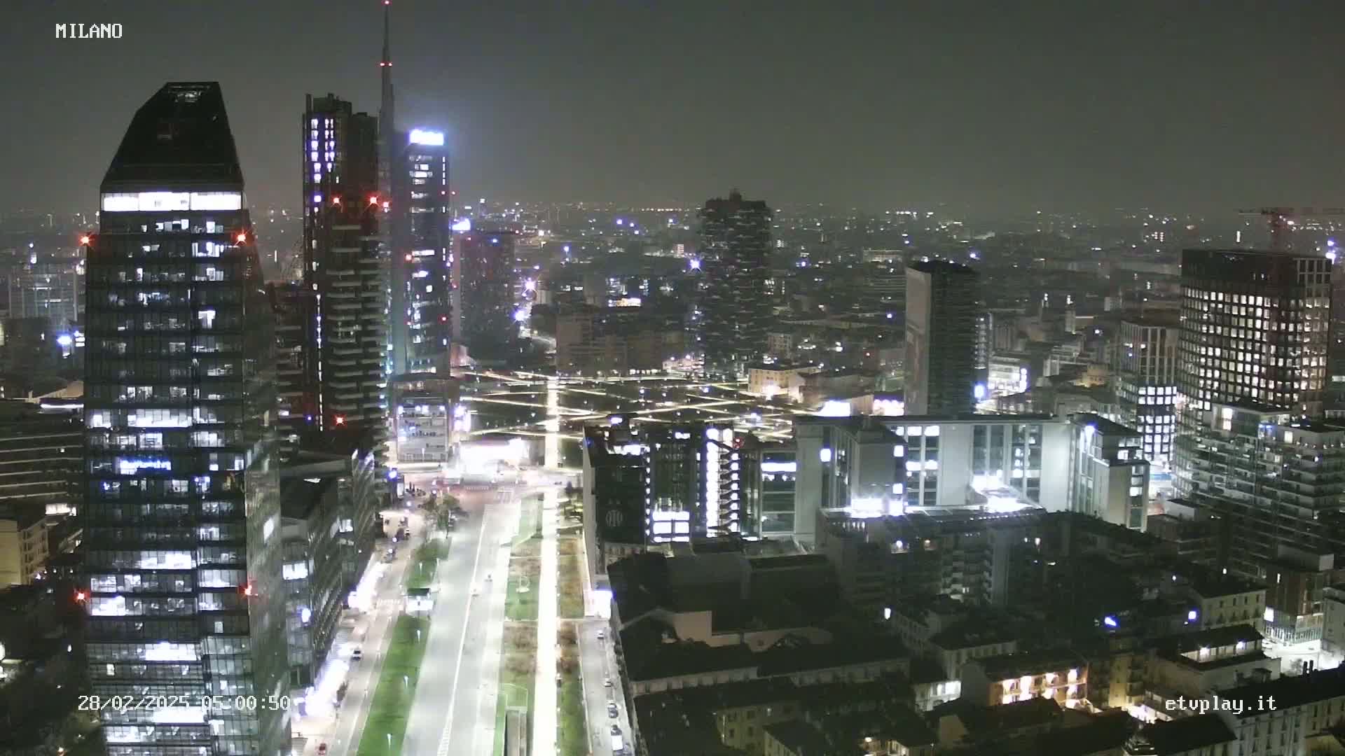 A nighttime aerial view of a city with many skyscrapers and illuminated streets under a dark, clear sky.