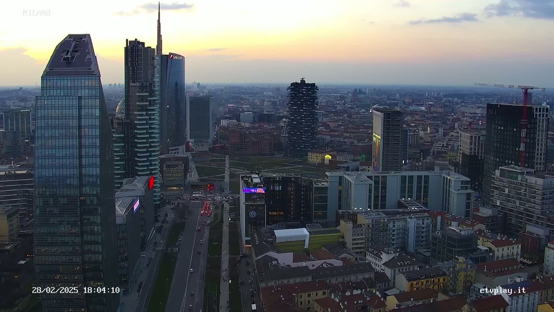 An aerial view of a city skyline at dusk, showing numerous skyscrapers and surrounding buildings, with a twilight sky.
