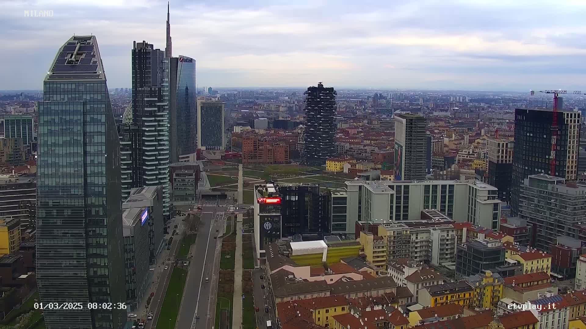 A high-angle, long shot of a city skyline on an overcast day, showing numerous skyscrapers and surrounding buildings.