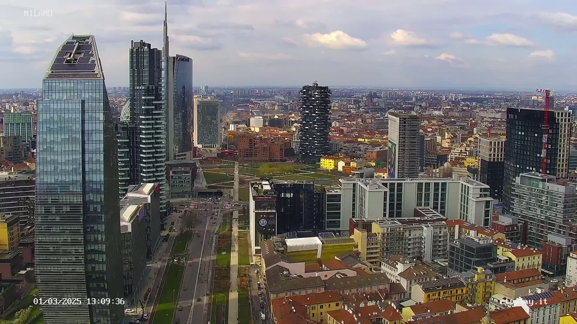 An aerial view of a city with numerous skyscrapers under a partly cloudy sky.