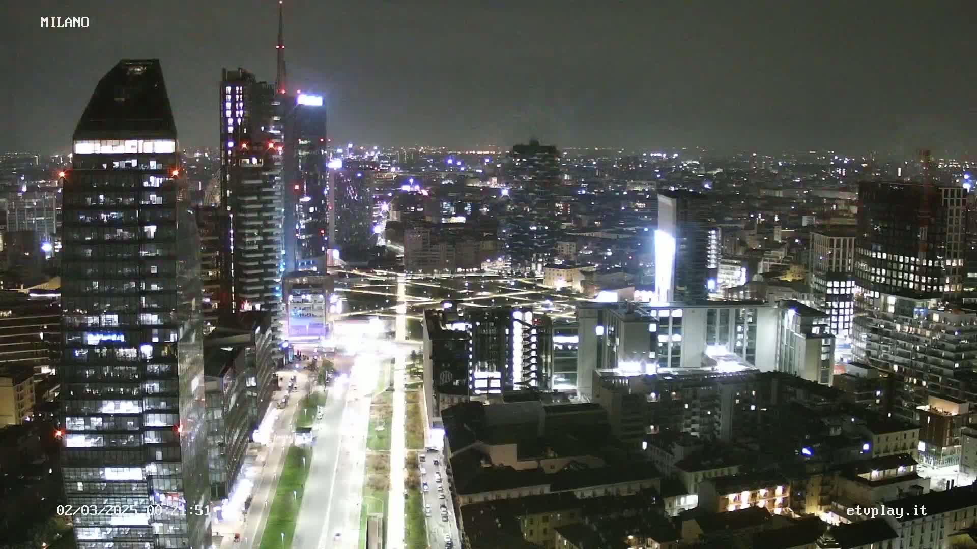 A nighttime aerial view of a city with numerous skyscrapers and illuminated streets, under a clear sky.