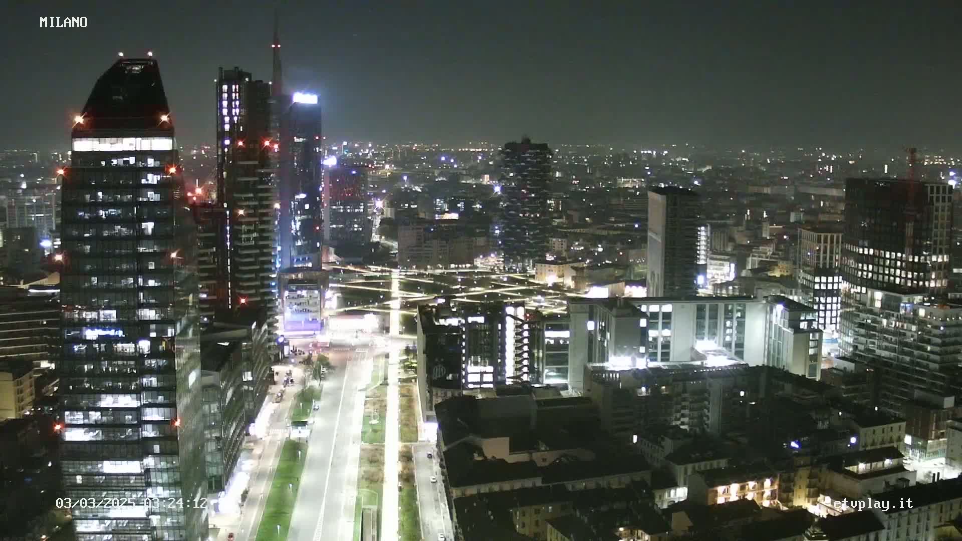 A nighttime aerial view of a city, showing numerous skyscrapers and buildings illuminated against a dark sky.