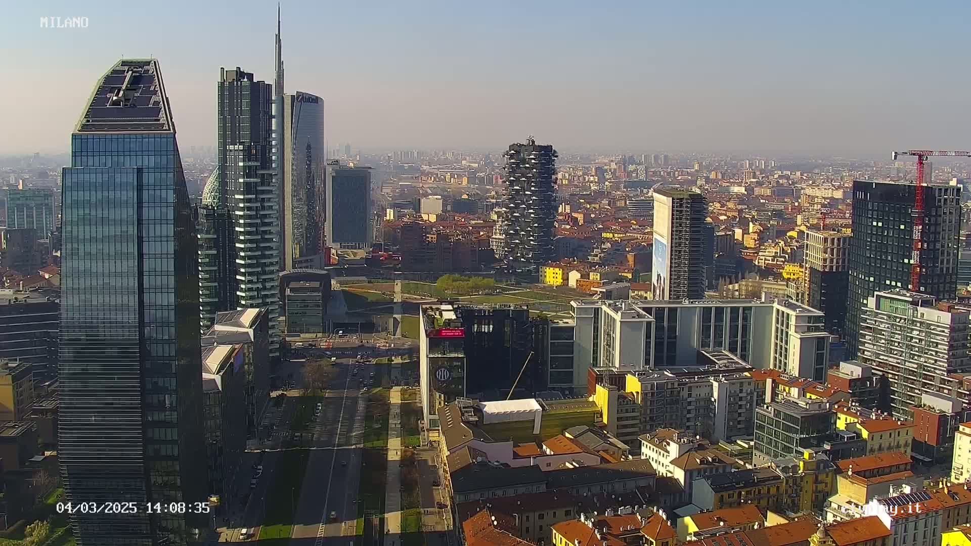 An aerial view of a city skyline on a clear, sunny day, showcasing numerous skyscrapers and surrounding buildings.
