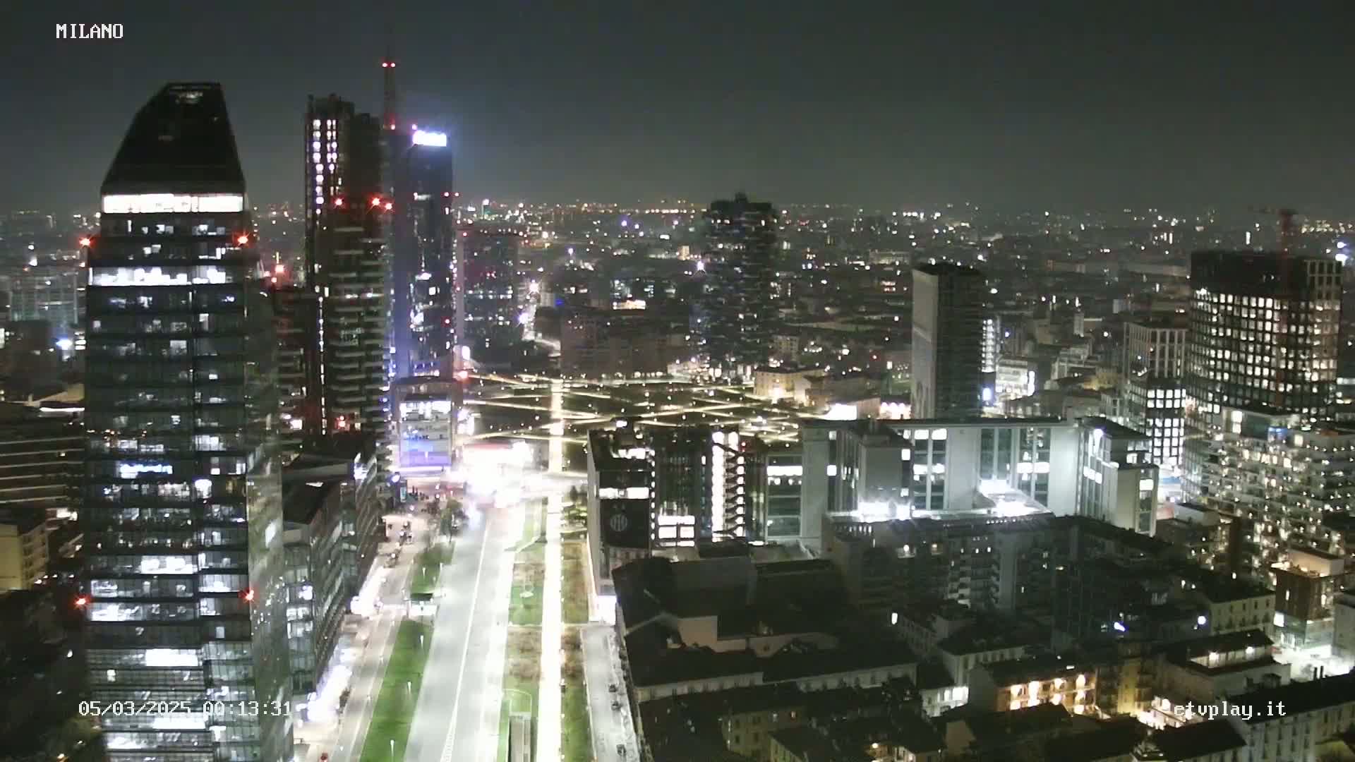 A nighttime aerial view of a city with numerous illuminated skyscrapers and buildings, stretching into the distance under a dark sky.