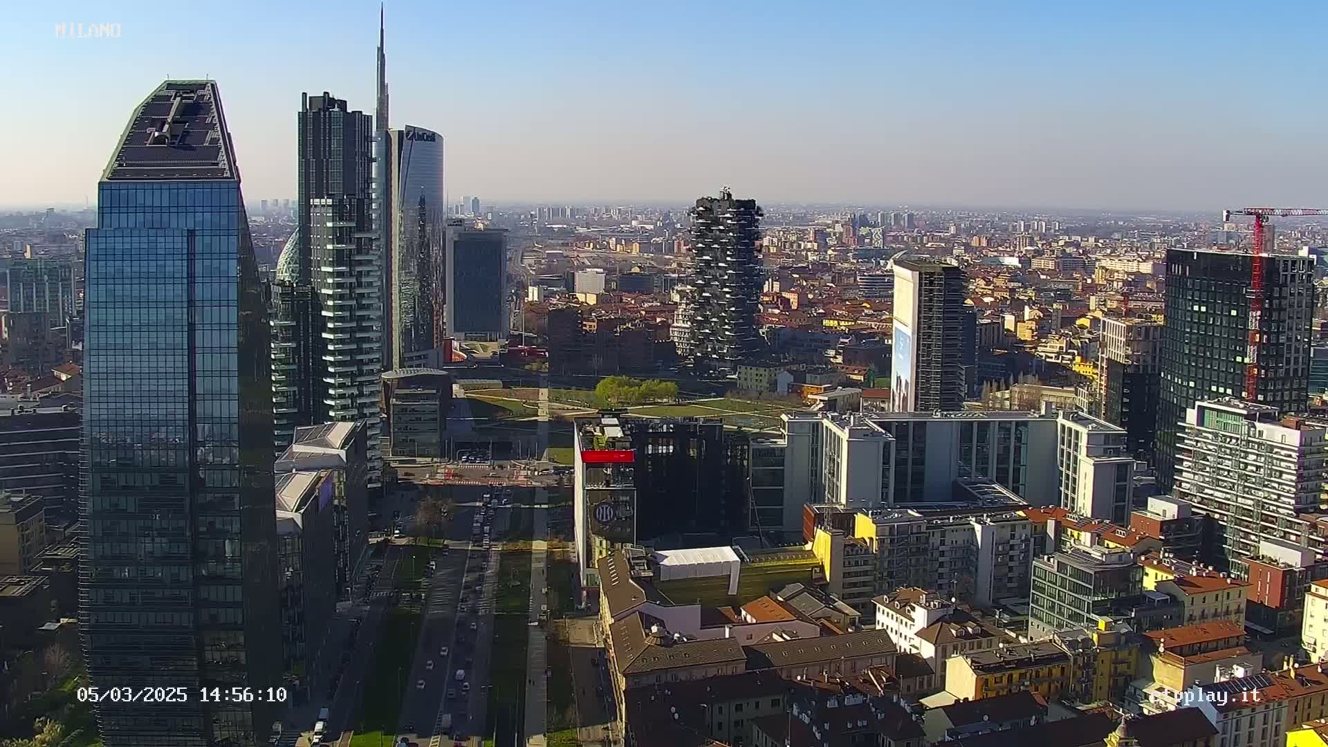 A high-angle, long shot of a dense cityscape featuring numerous skyscrapers under a clear, sunny sky.