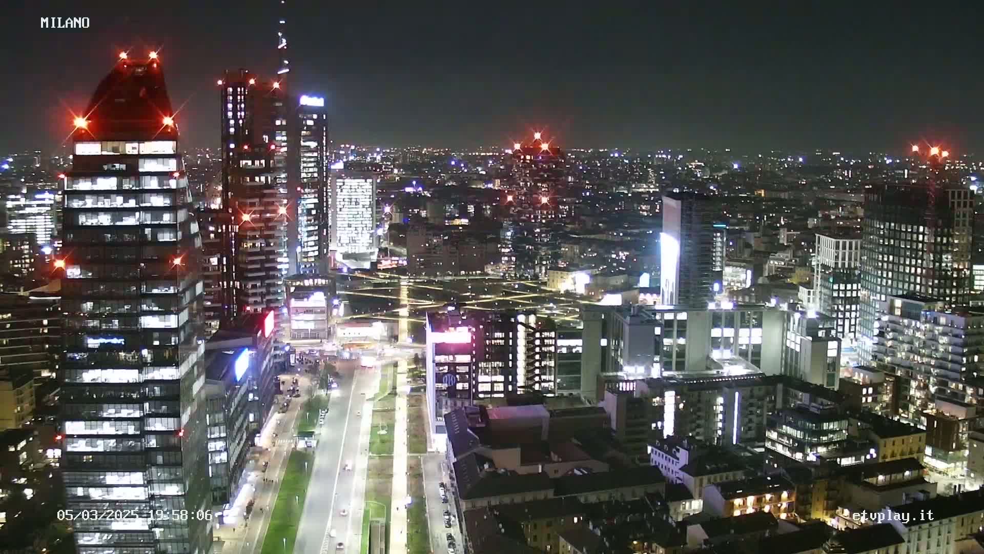 A nighttime aerial view of a city, showing brightly lit skyscrapers and streets, under a clear sky.