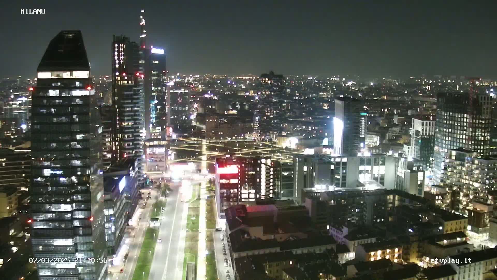 A nighttime aerial view of a city's illuminated skyline, showcasing numerous skyscrapers and city streets.