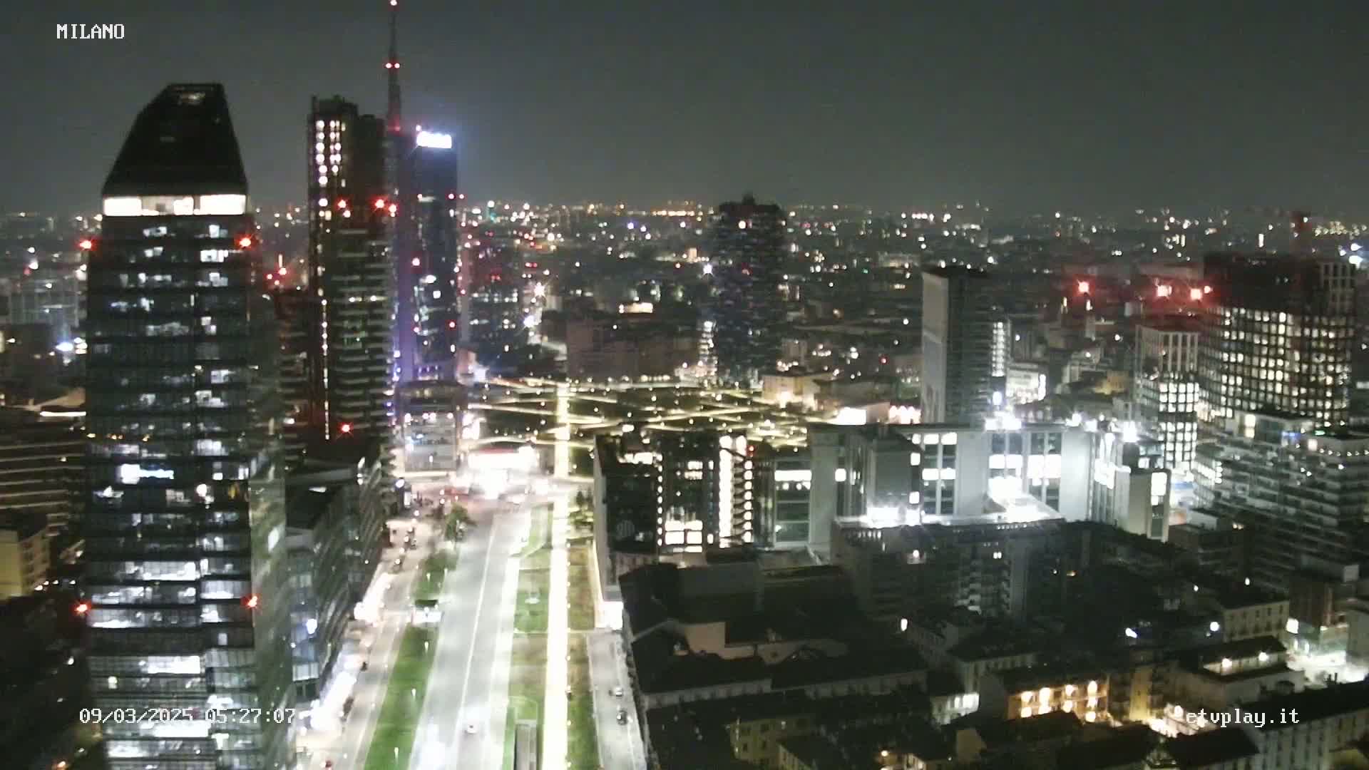 A nighttime aerial view of a city with numerous skyscrapers illuminated, showcasing a clear sky.