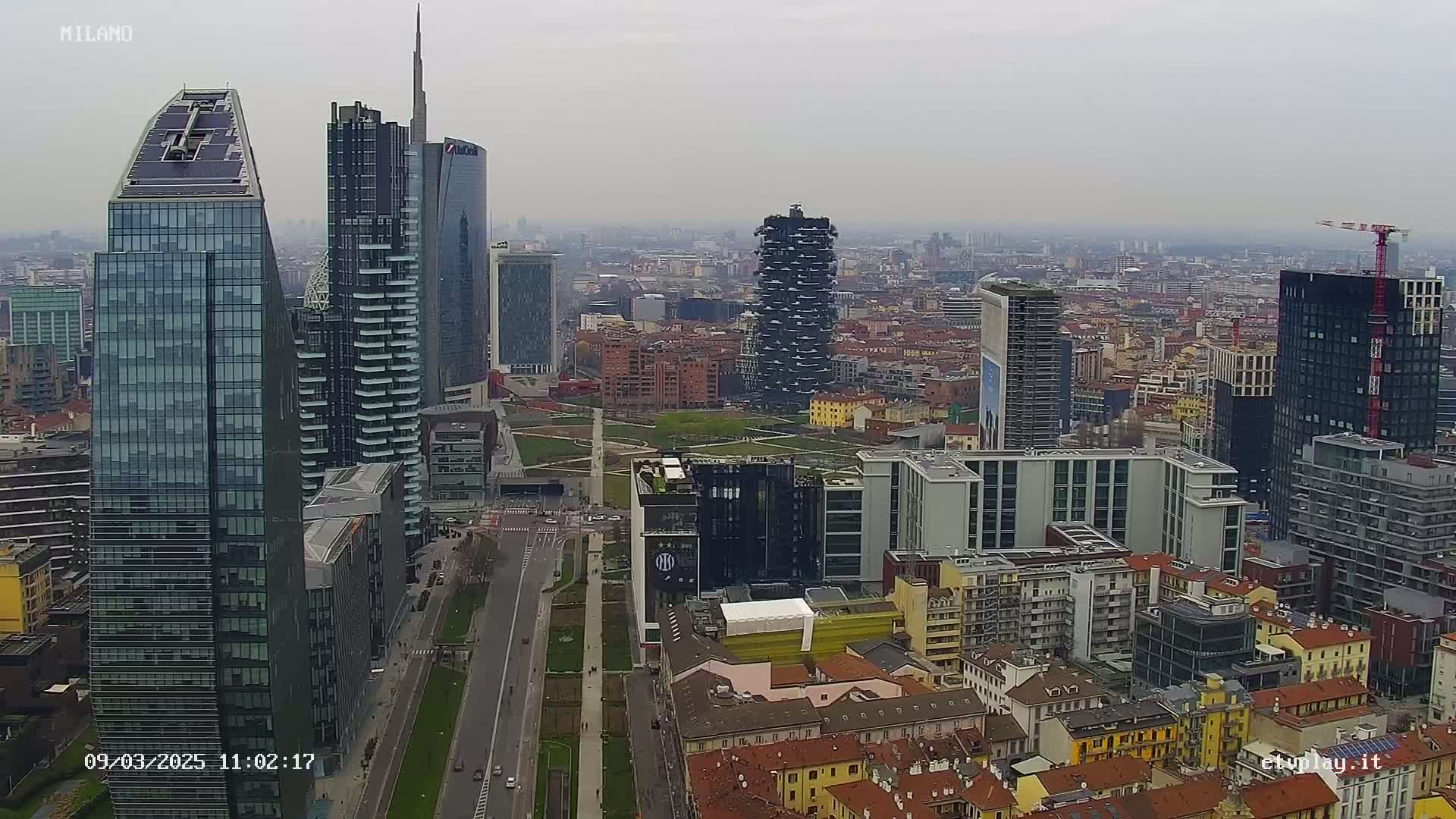 An aerial view of a city skyline on an overcast day, showcasing numerous modern skyscrapers and surrounding low-rise buildings.