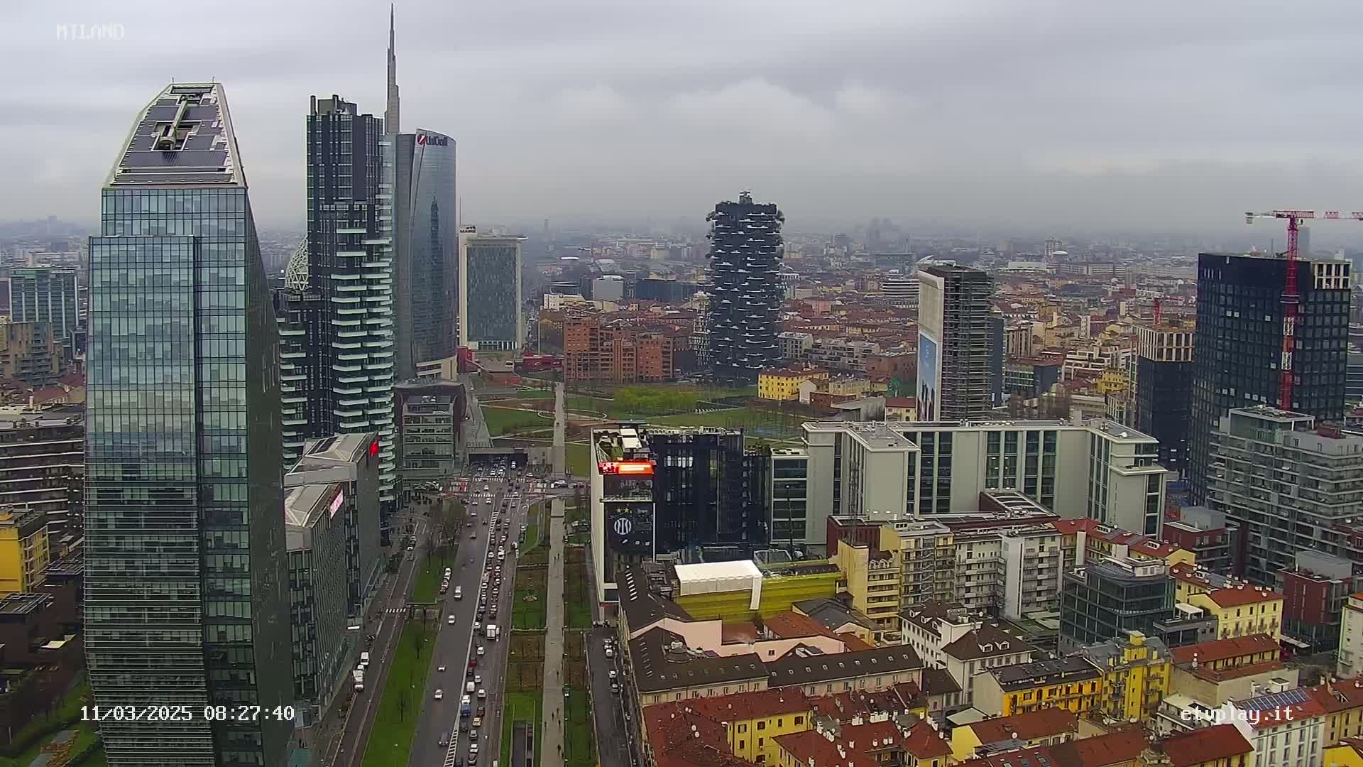 A high-angle view of a city skyline under an overcast sky, showing numerous skyscrapers and surrounding buildings.